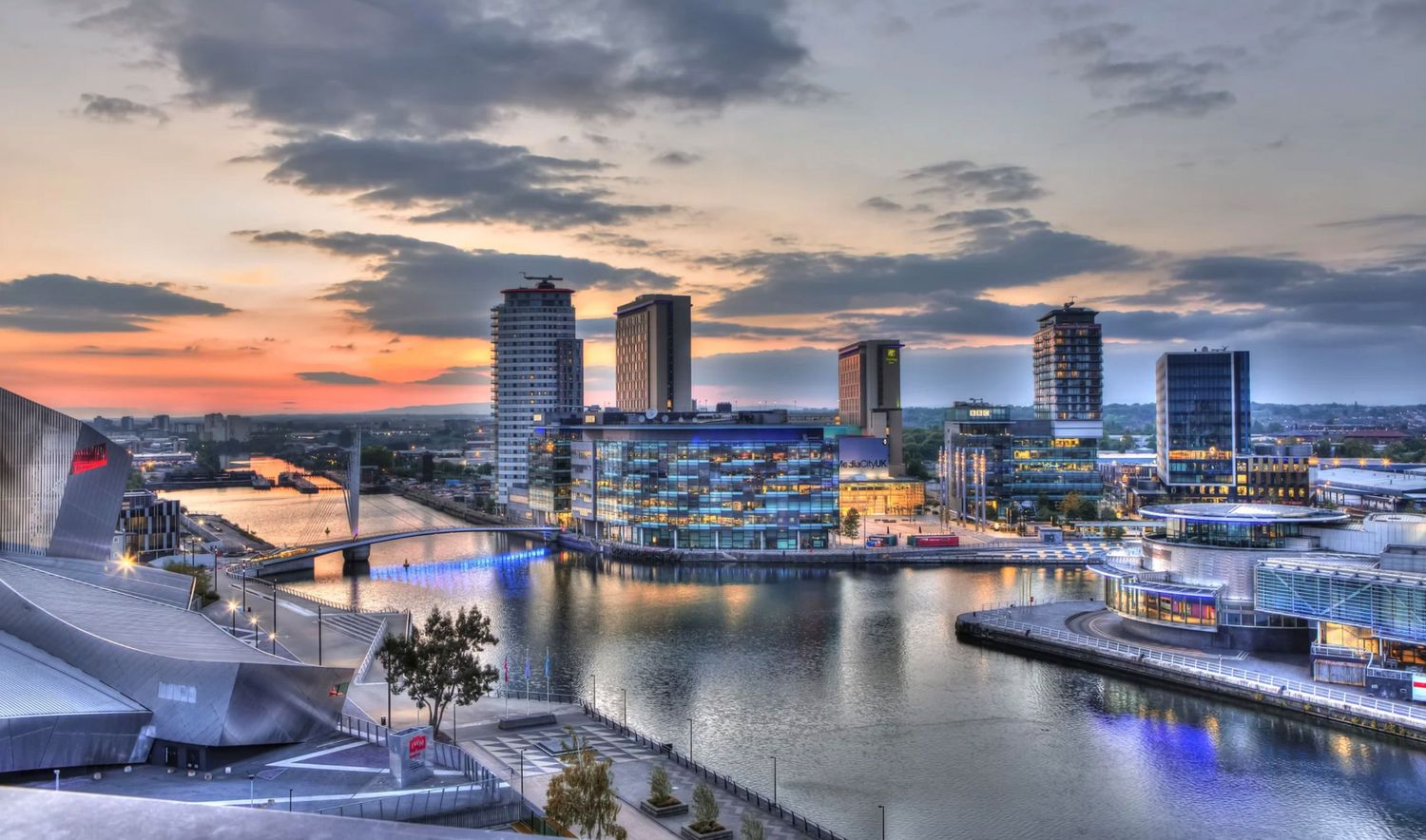 Stunning HDR sunset cityscape of MediaCityUK Salford Quays with reflections on the water and modern skyscrapers.