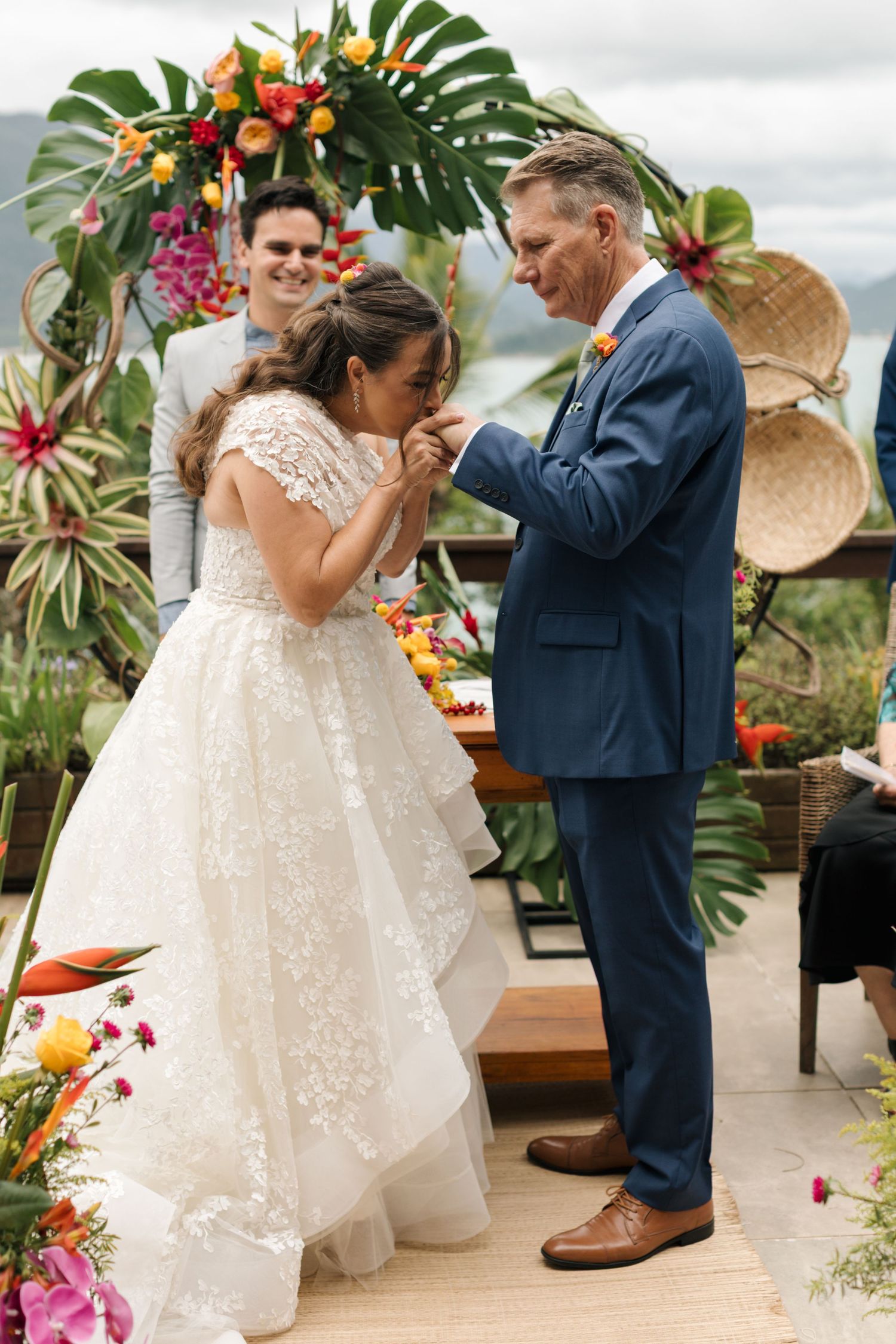 A couple shares their first dance on a tropical terrace decorated with monstera leaves and bright flowers.