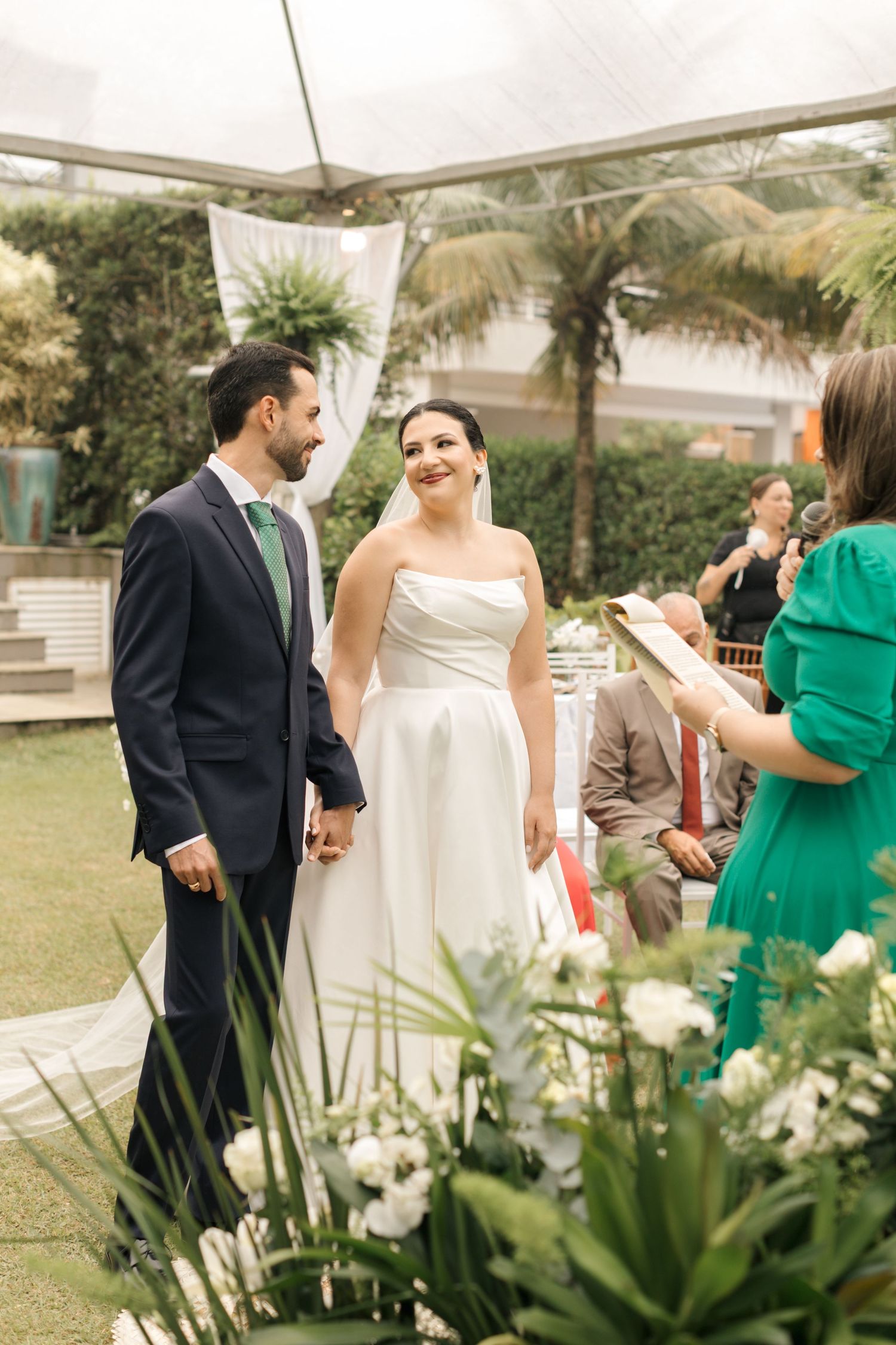 Wedding party gathered outdoors with tropical palm trees and white floral decorations.