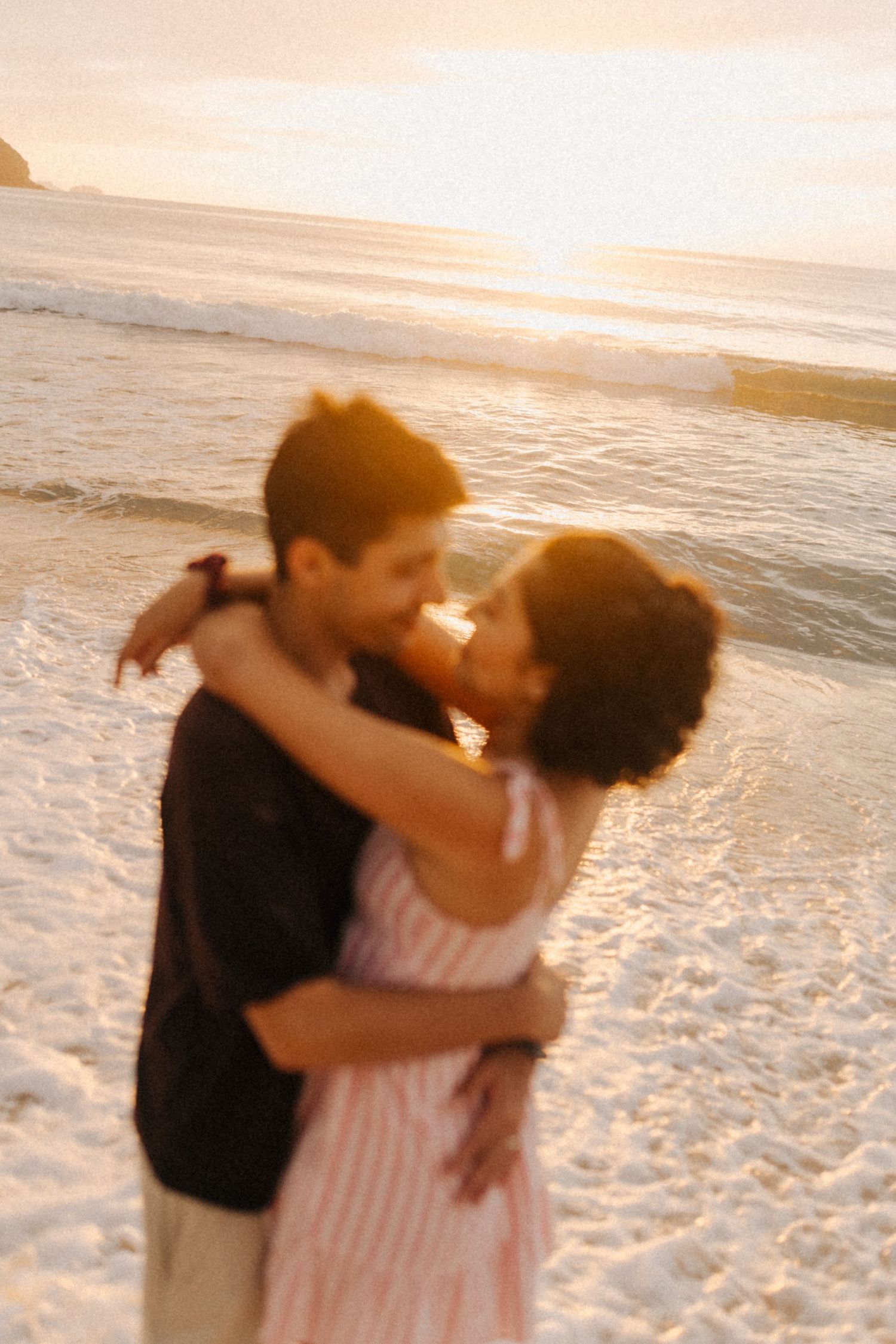 Cena romântica da praia do pôr do sol com casal abraçando em suave luz dourada na costa arenosa.