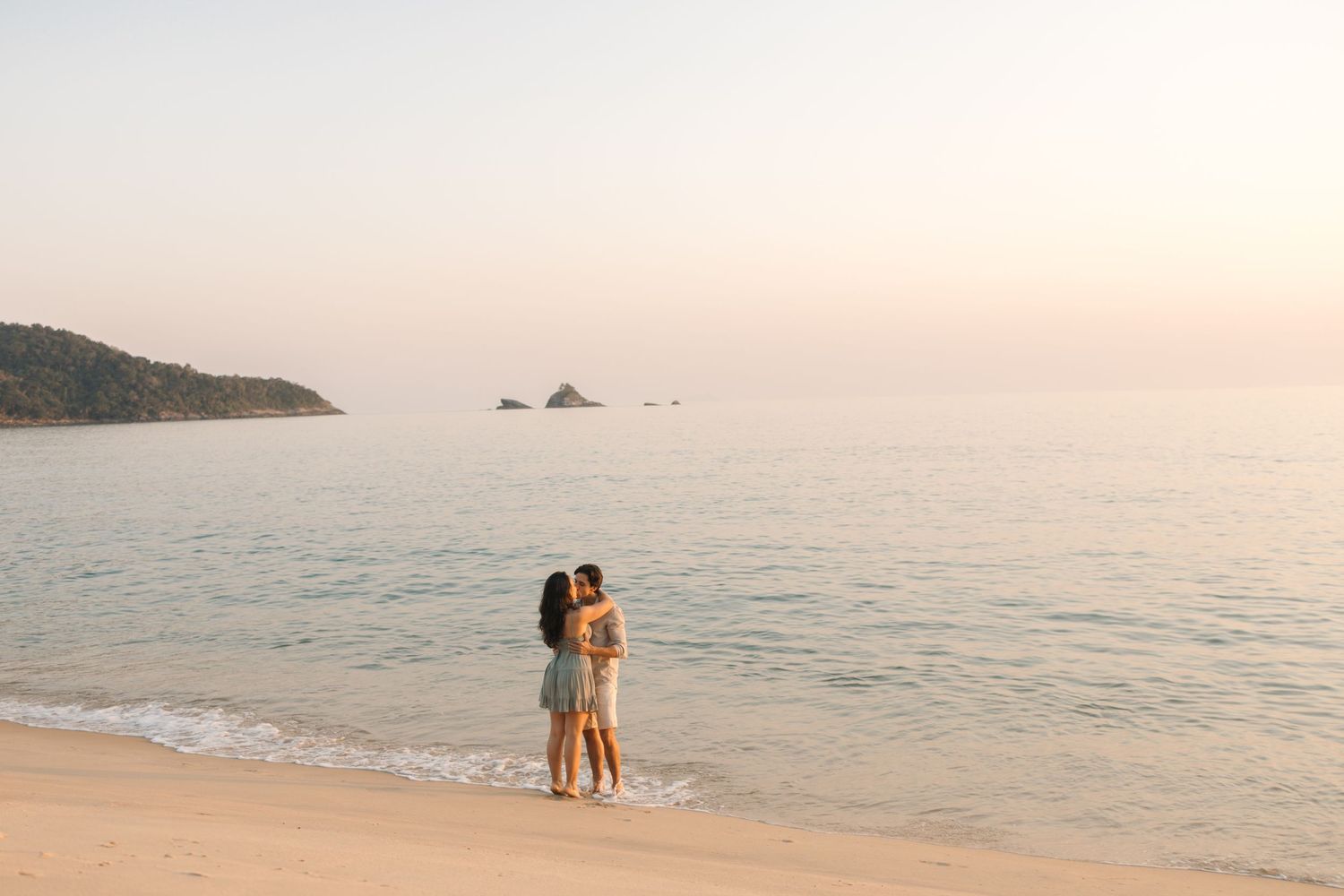 Silhouettes of two people standing on a beach at dusk with distant islands on the horizon.