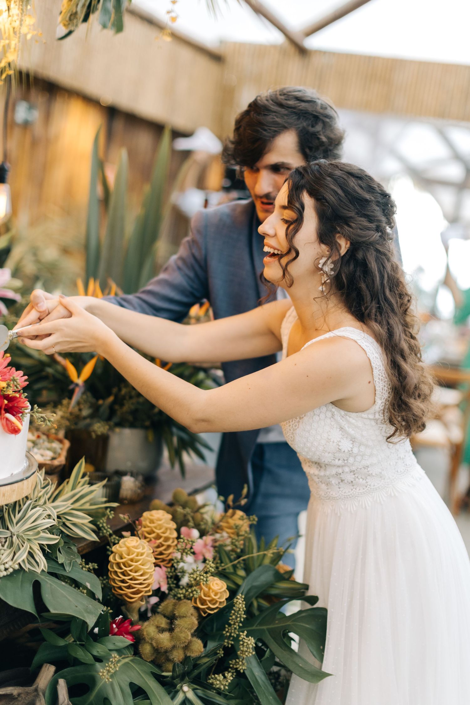 A couple celebrates at a tropical-themed wedding reception with lush greenery and pinecone decorations.