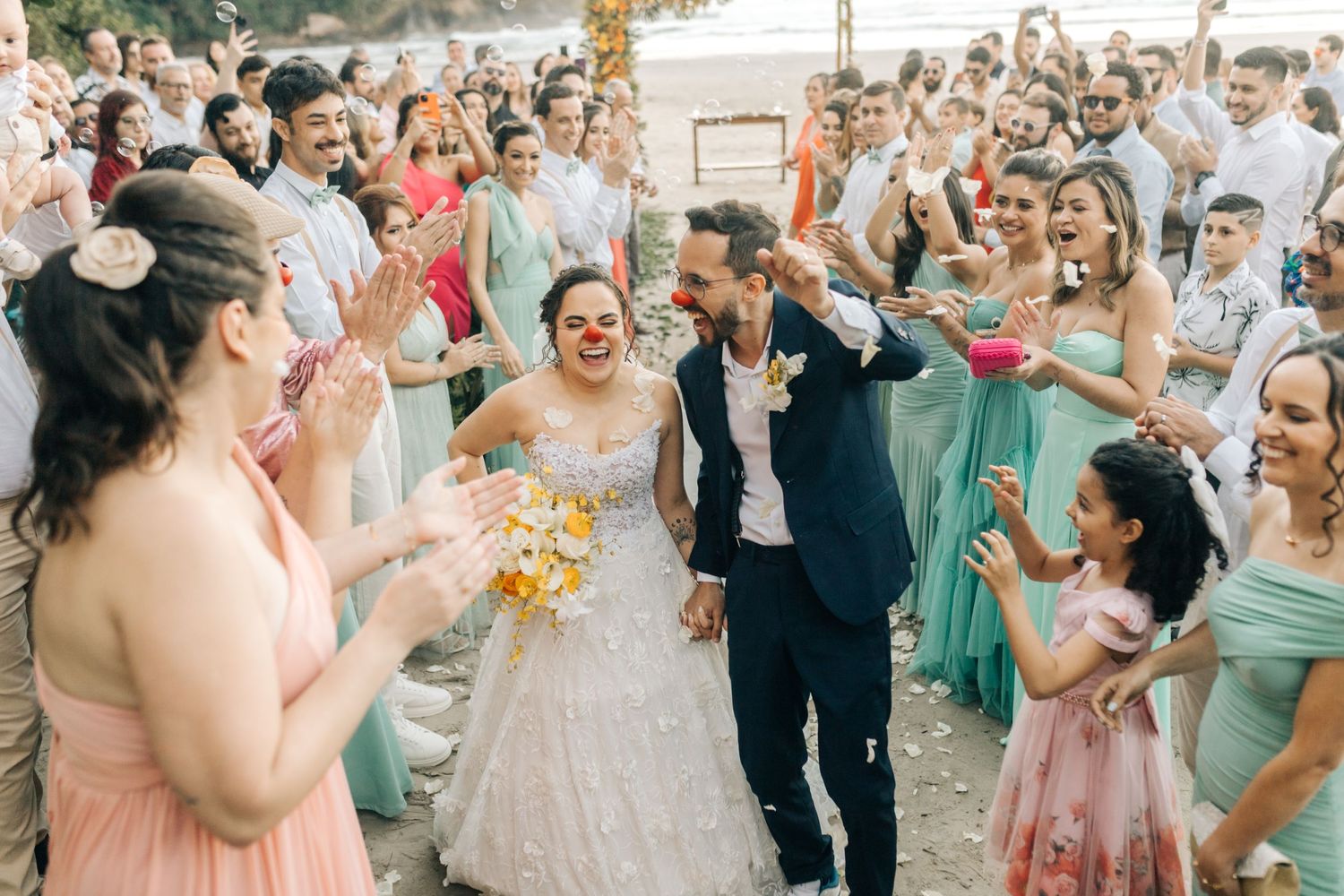 Wedding party celebrates with confetti throwing on a beach in matching mint green bridesmaid dresses.