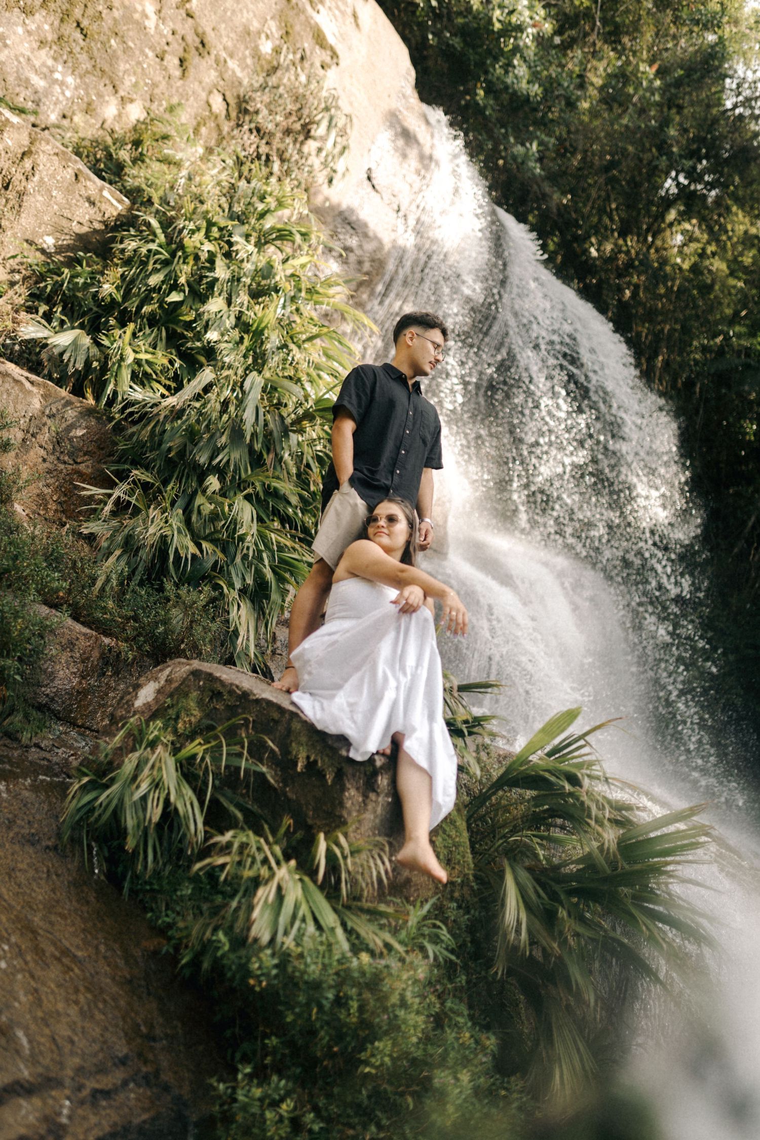 A romantic portrait by a cascading waterfall with lush tropical foliage framing the scene.