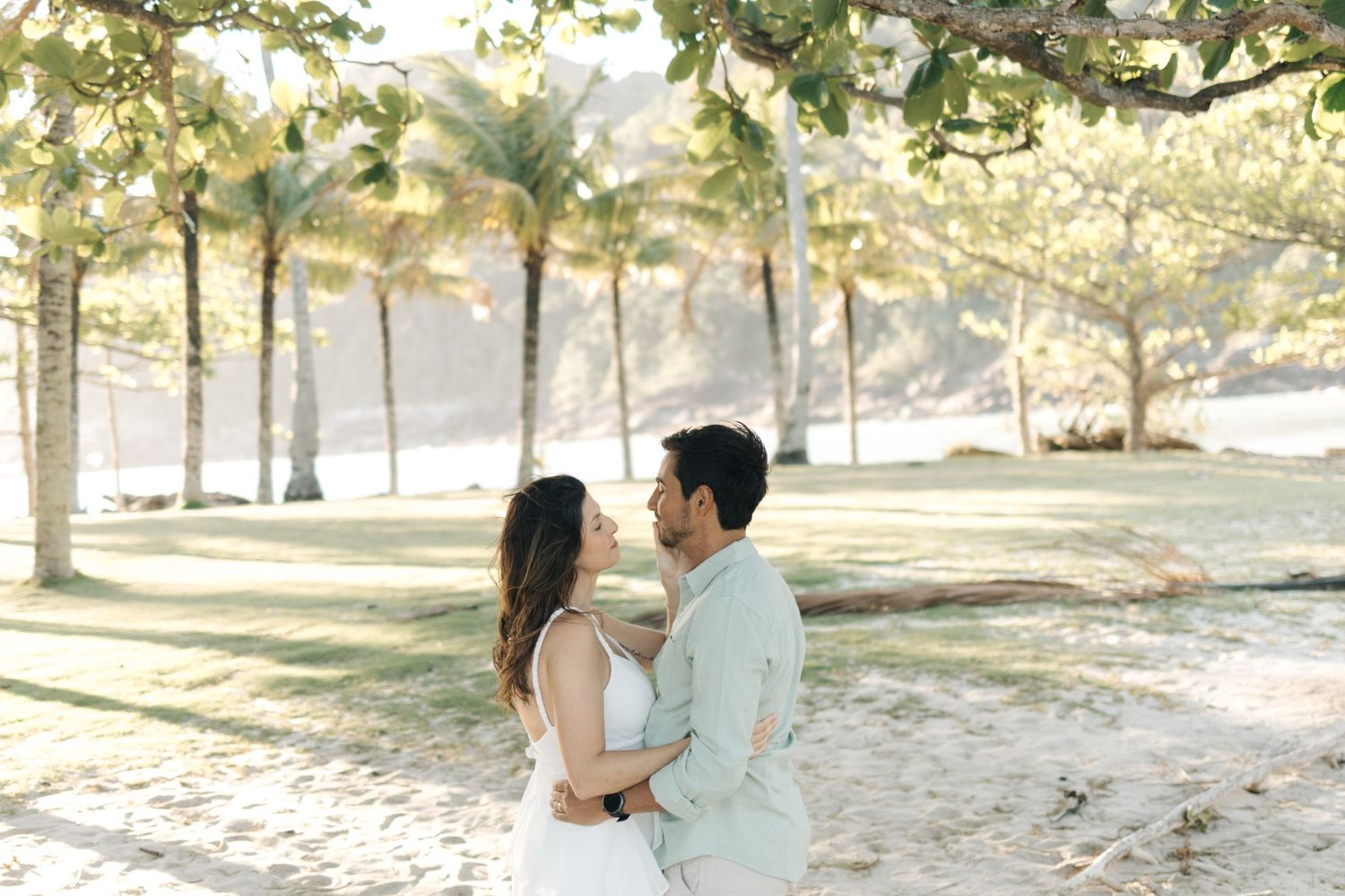 A couple enjoys a romantic moment together in a sunlit park setting with trees in the background.