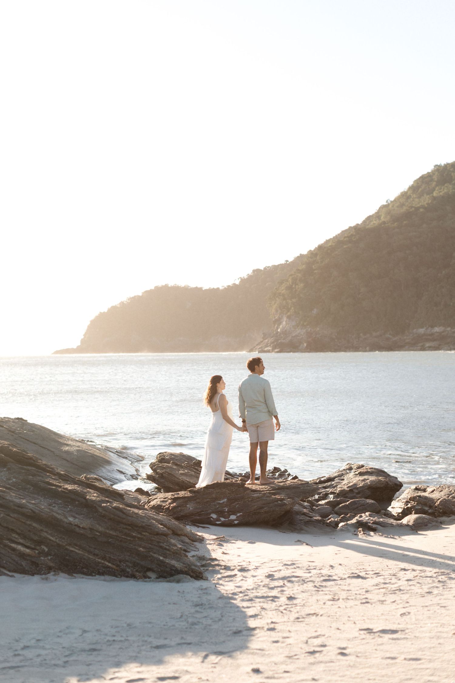 A couple enjoying a peaceful moment on a rocky beach overlooking the ocean at golden hour.