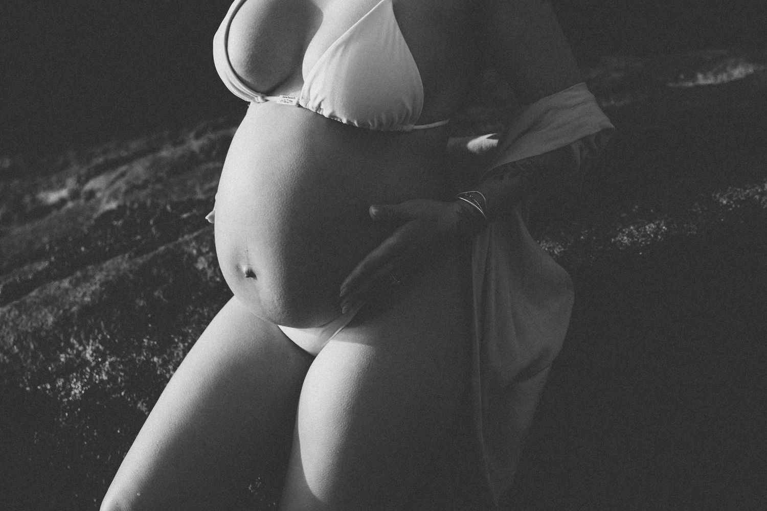 Artistic black and white maternity photo highlighting pregnancy silhouette against dark background.