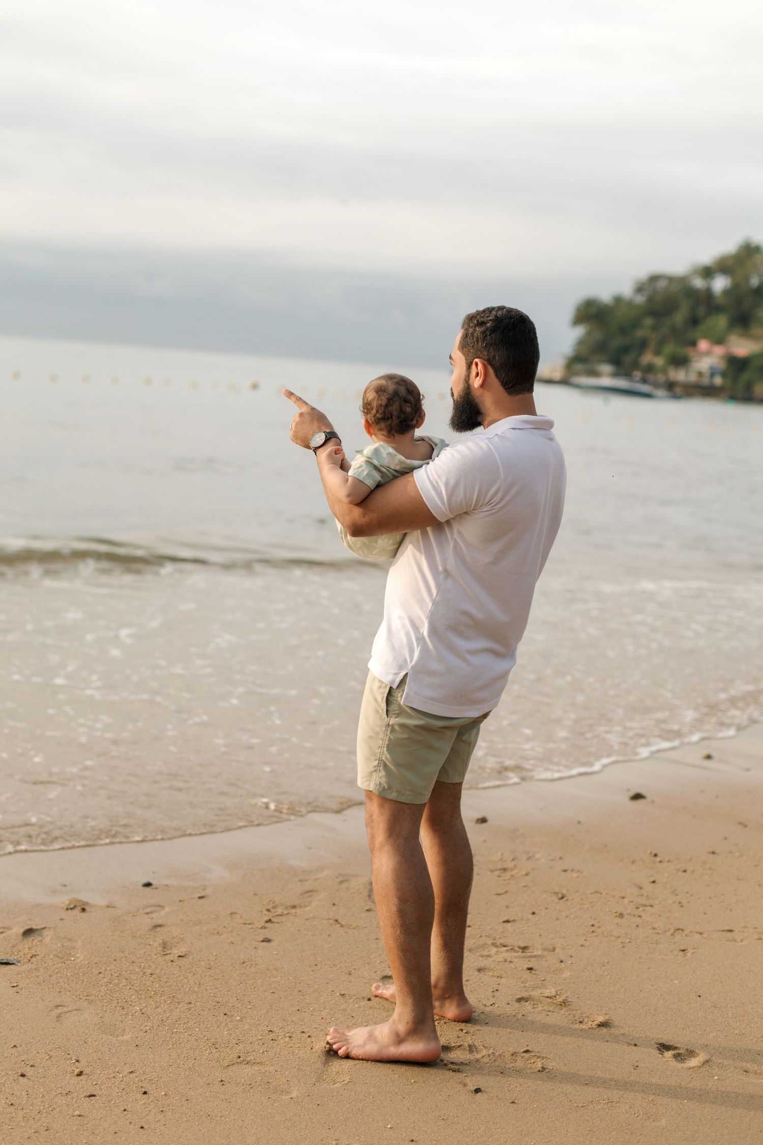Two people standing at the edge of the ocean pointing towards something in the distance.