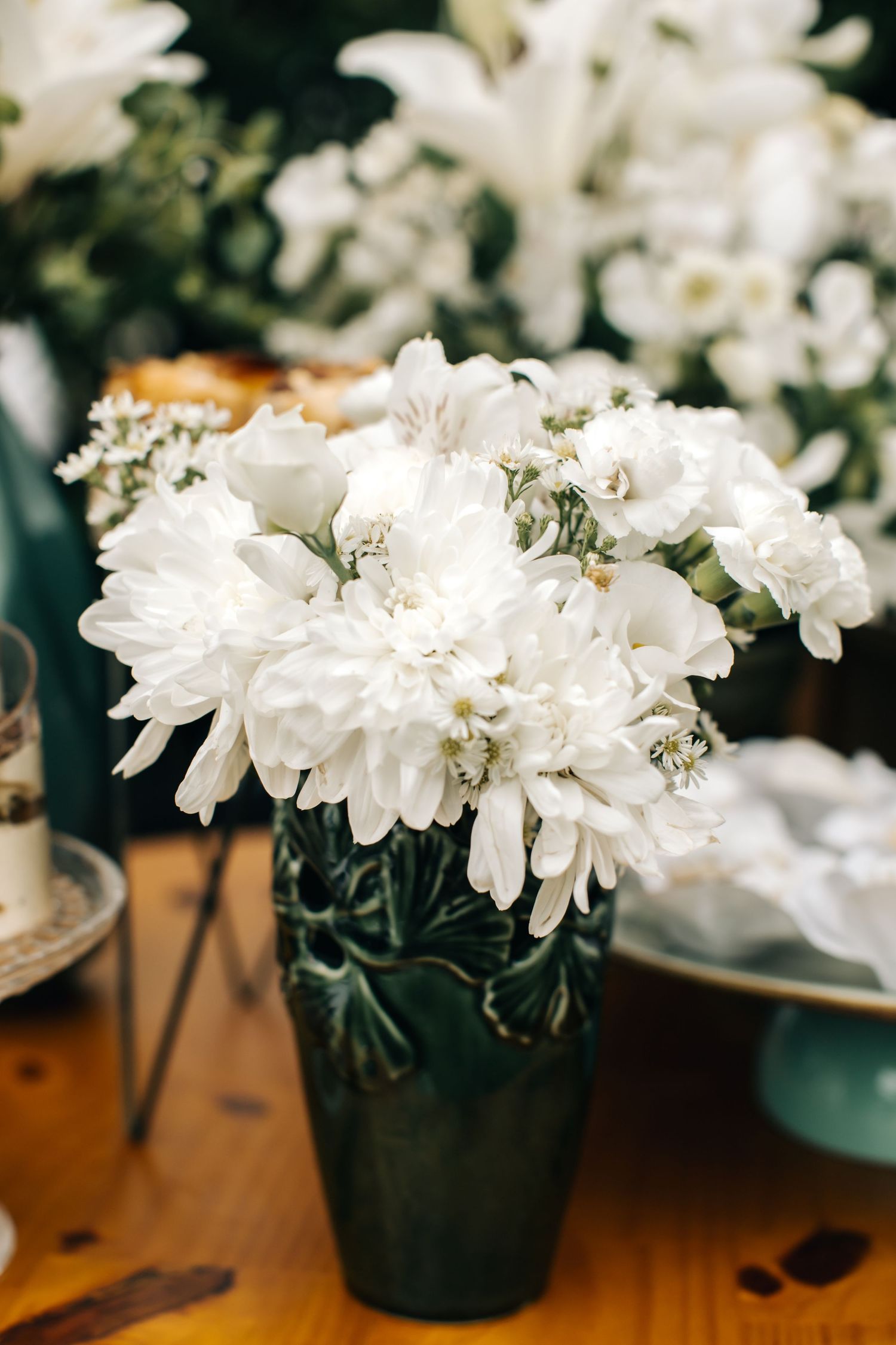 White chrysanthemums and flowers arranged in dark containers on a wooden surface.