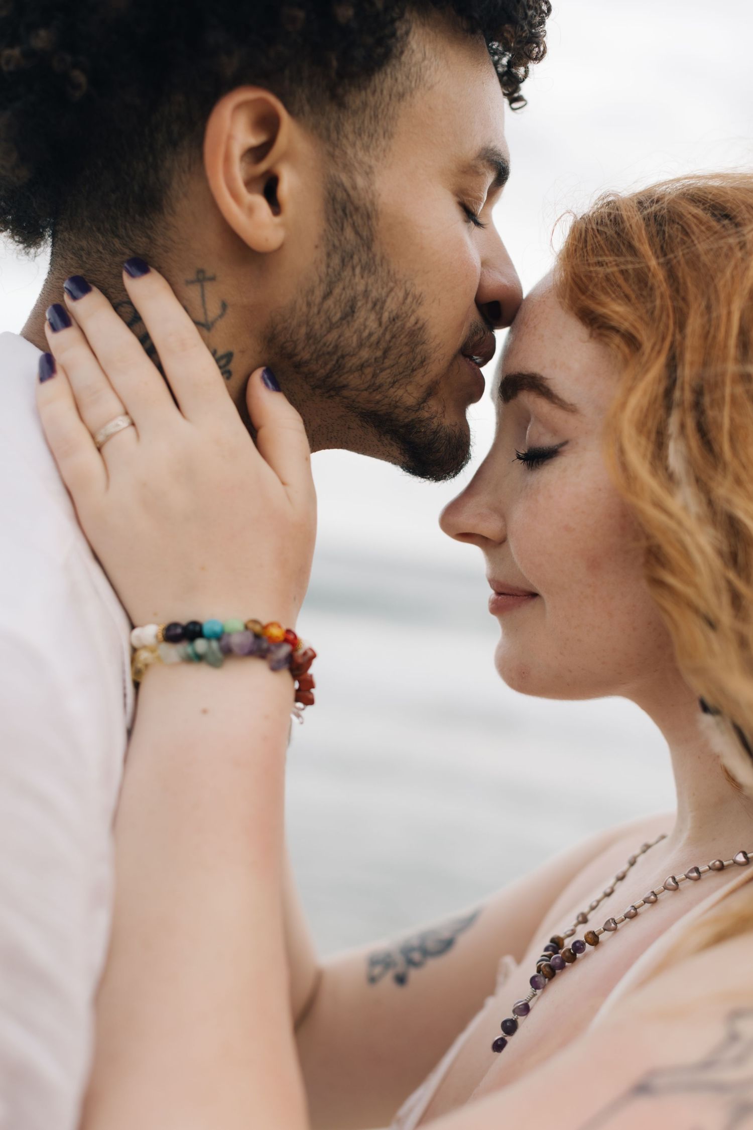 A tender close-up moment between a couple wearing white clothing against an ocean backdrop.