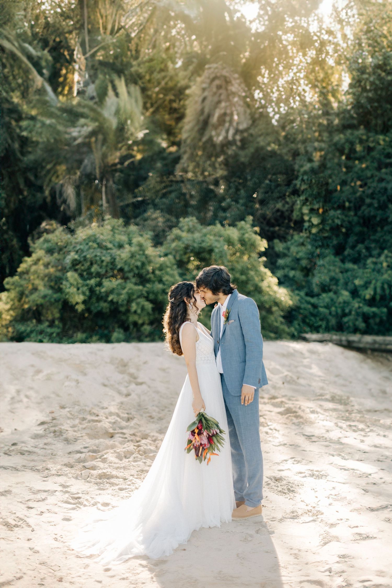 Golden hour wedding photos of couple on sandy beach with lush tropical background.