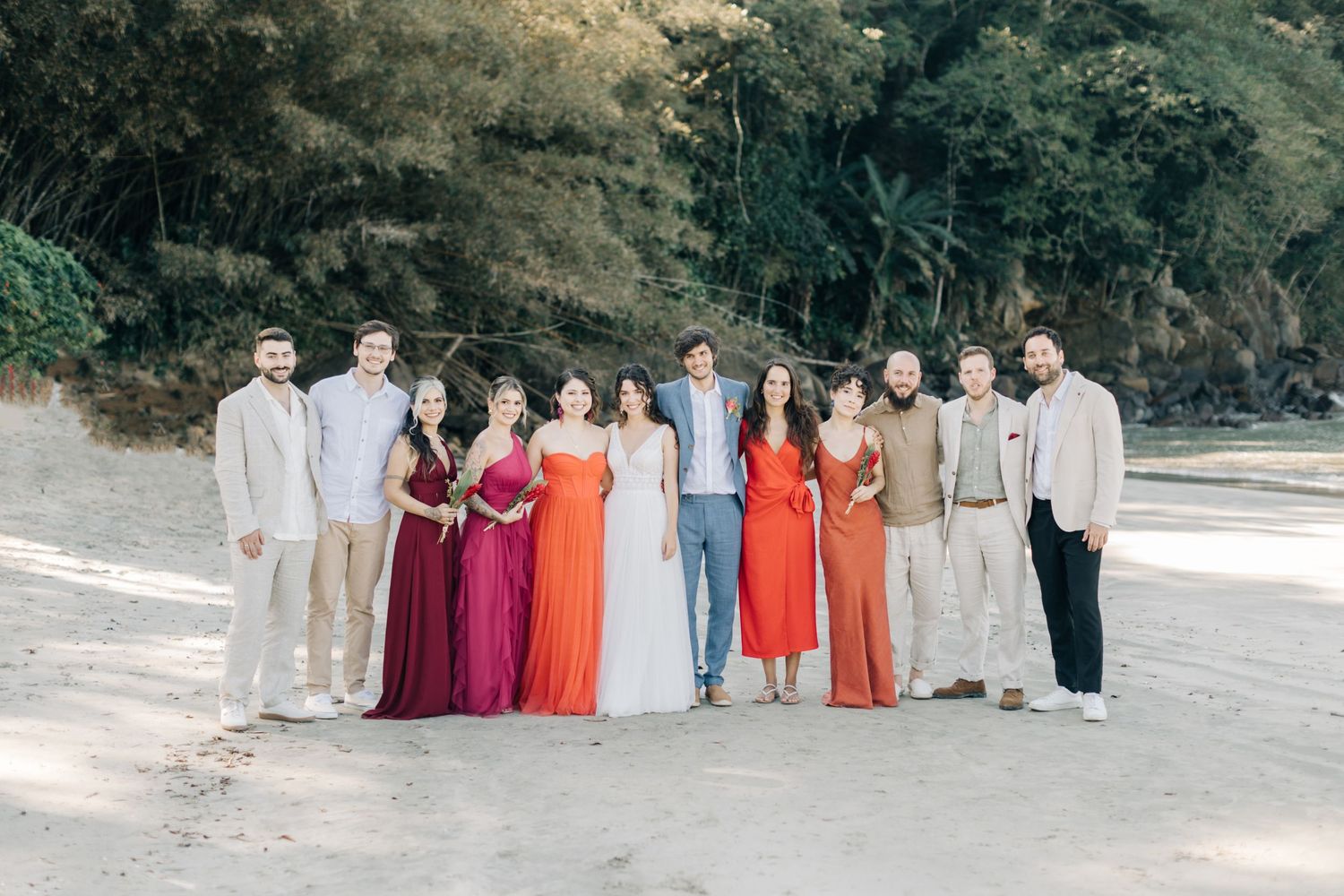 Wedding party members lined up on a beach with mountains in the background.
