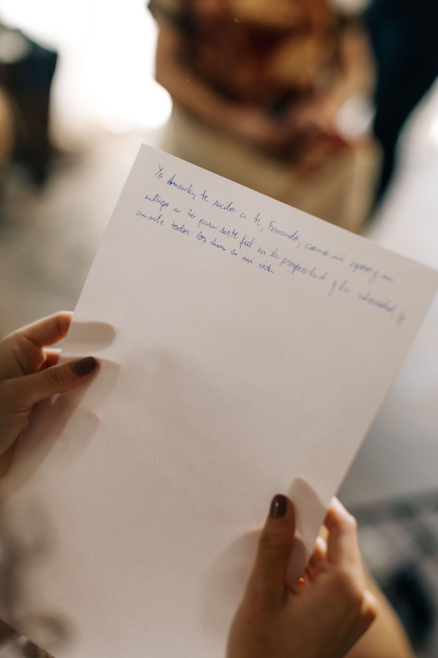 Hands holding a handwritten note on white paper in an indoor setting.