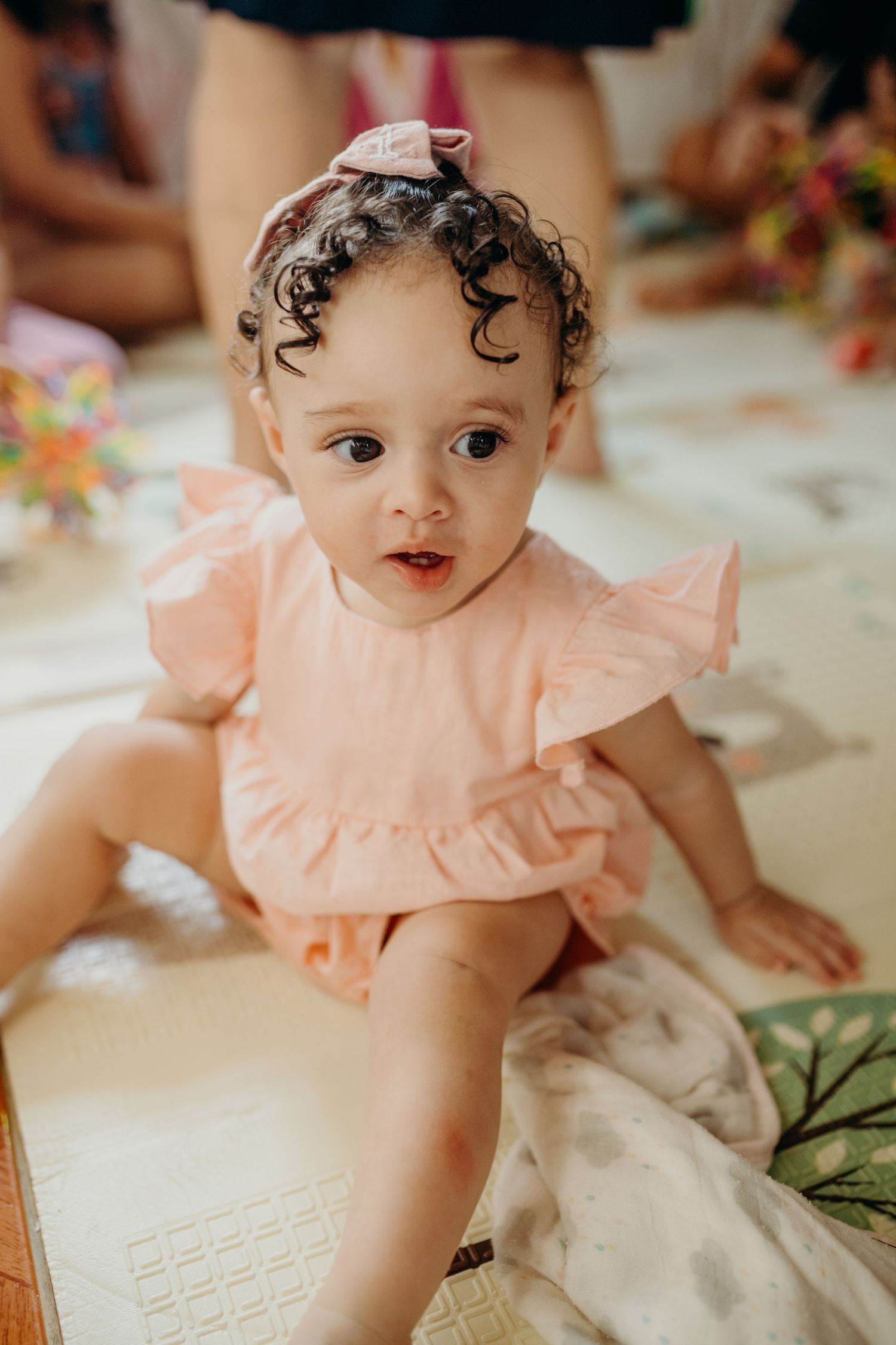 Baby wearing a peach-colored ruffled outfit plays on a patterned mat.