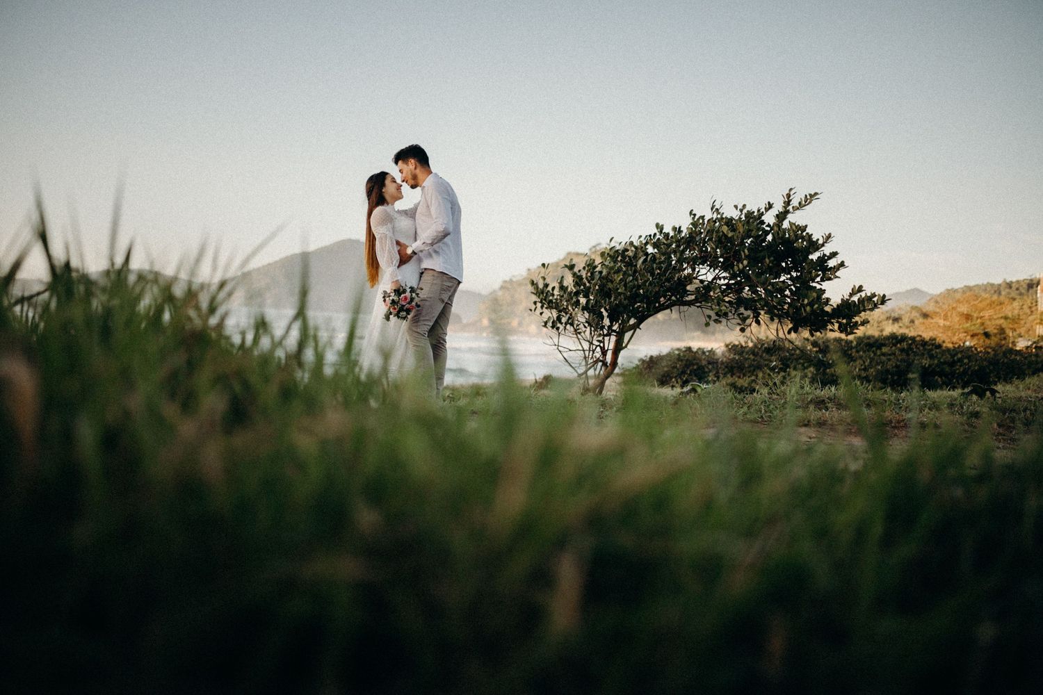 Wide landscape shot of couple silhouetted against coastal scenery.