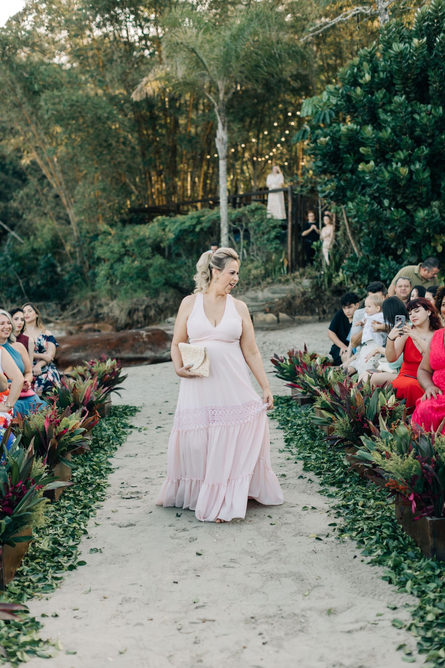 Bridesmaids in light pink dresses walking down a sandy aisle at an outdoor ceremony.