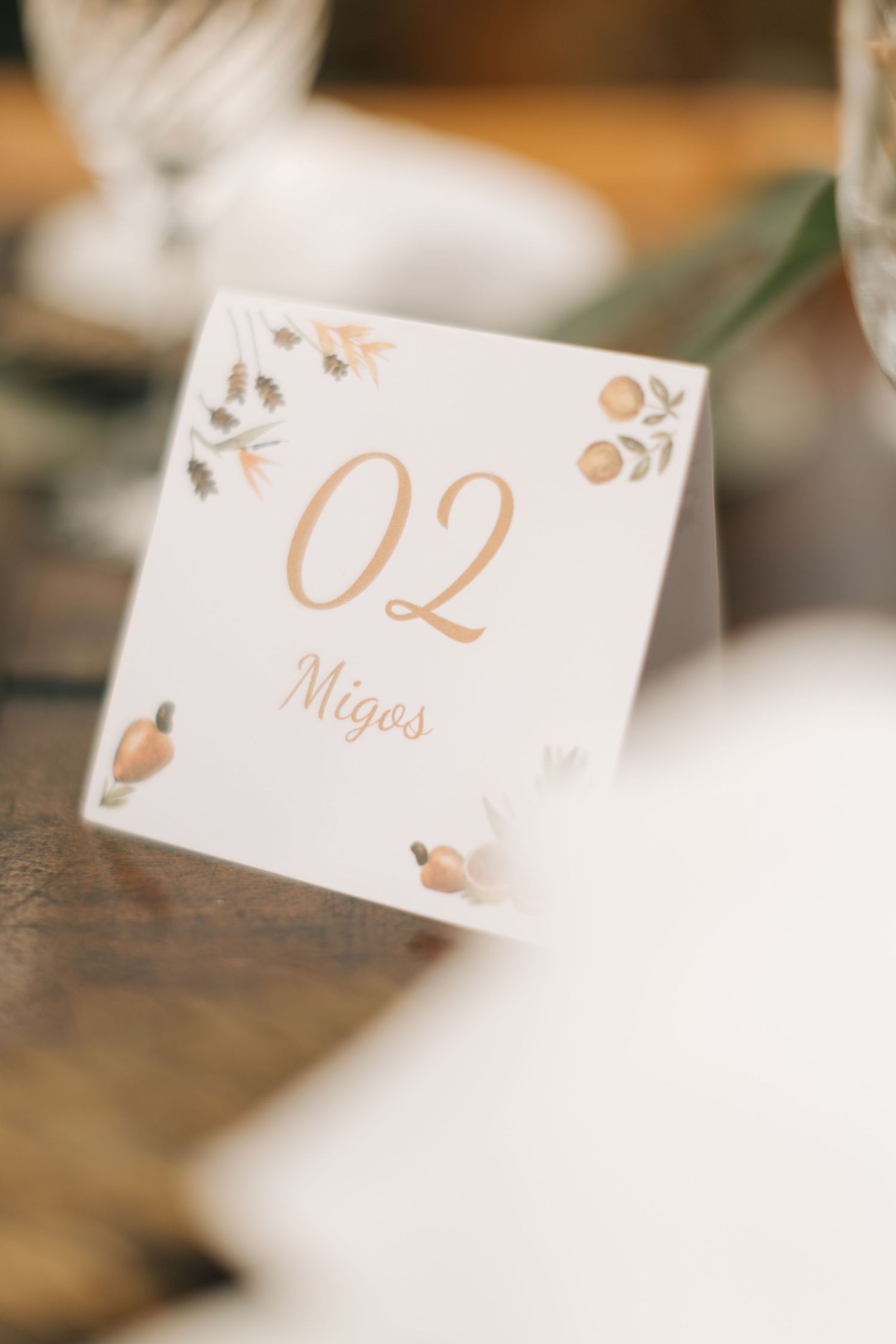 Close-up of a white table number card with delicate floral details and gold text.