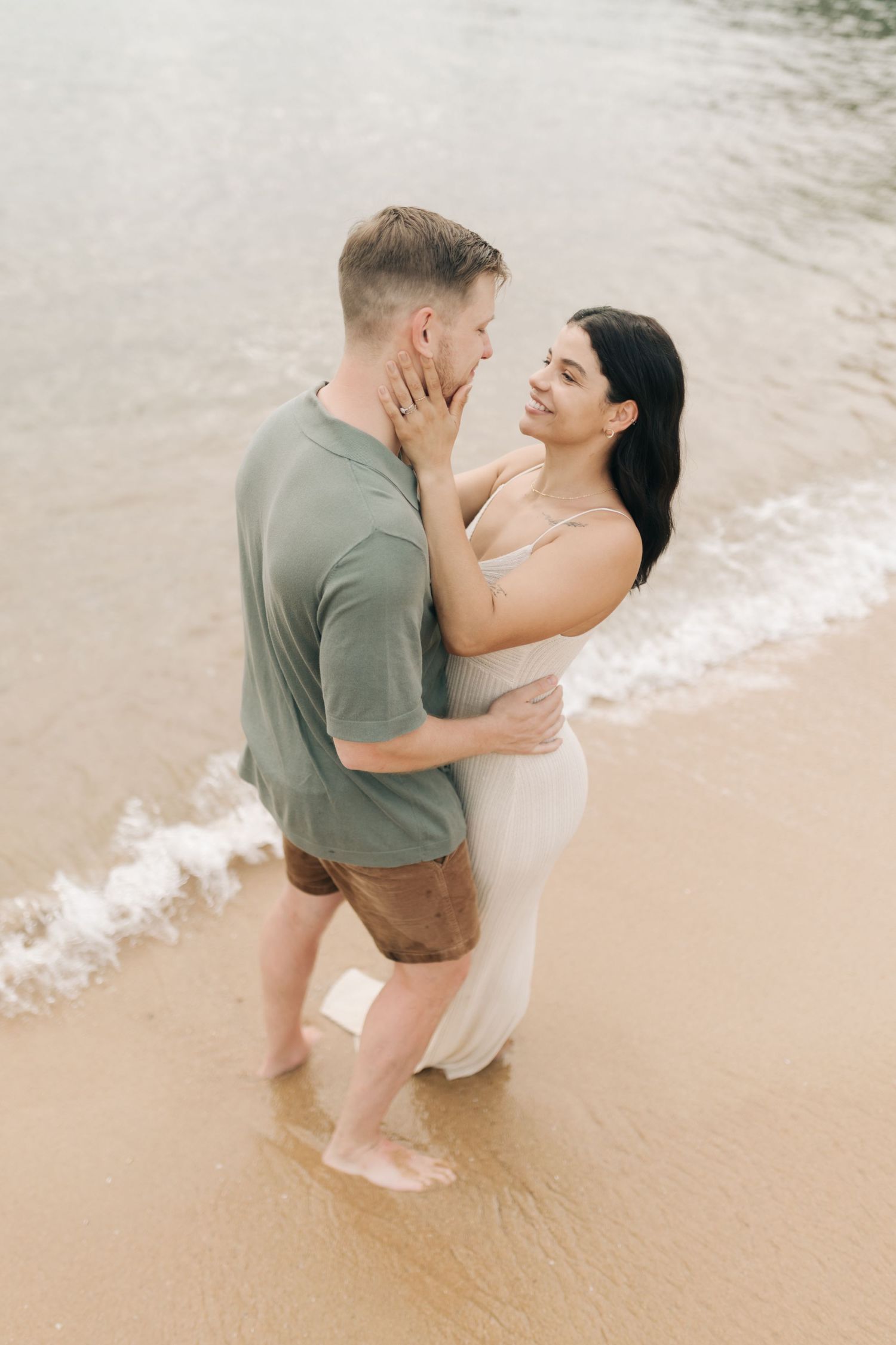 A tender moment between a couple embracing on a beach with gentle waves in the background.
