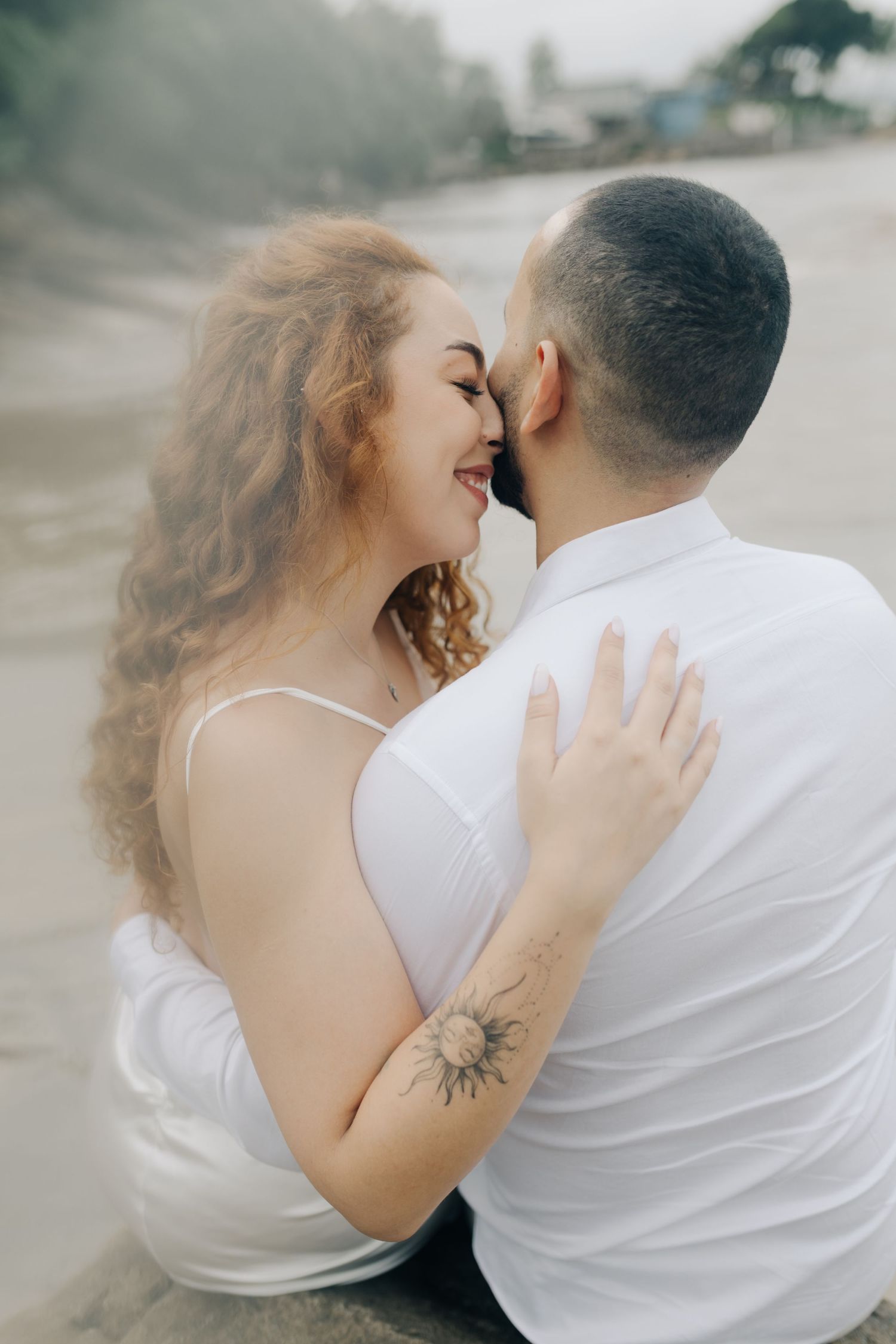 Intimate beachside portrait of couple touching foreheads and smiling.