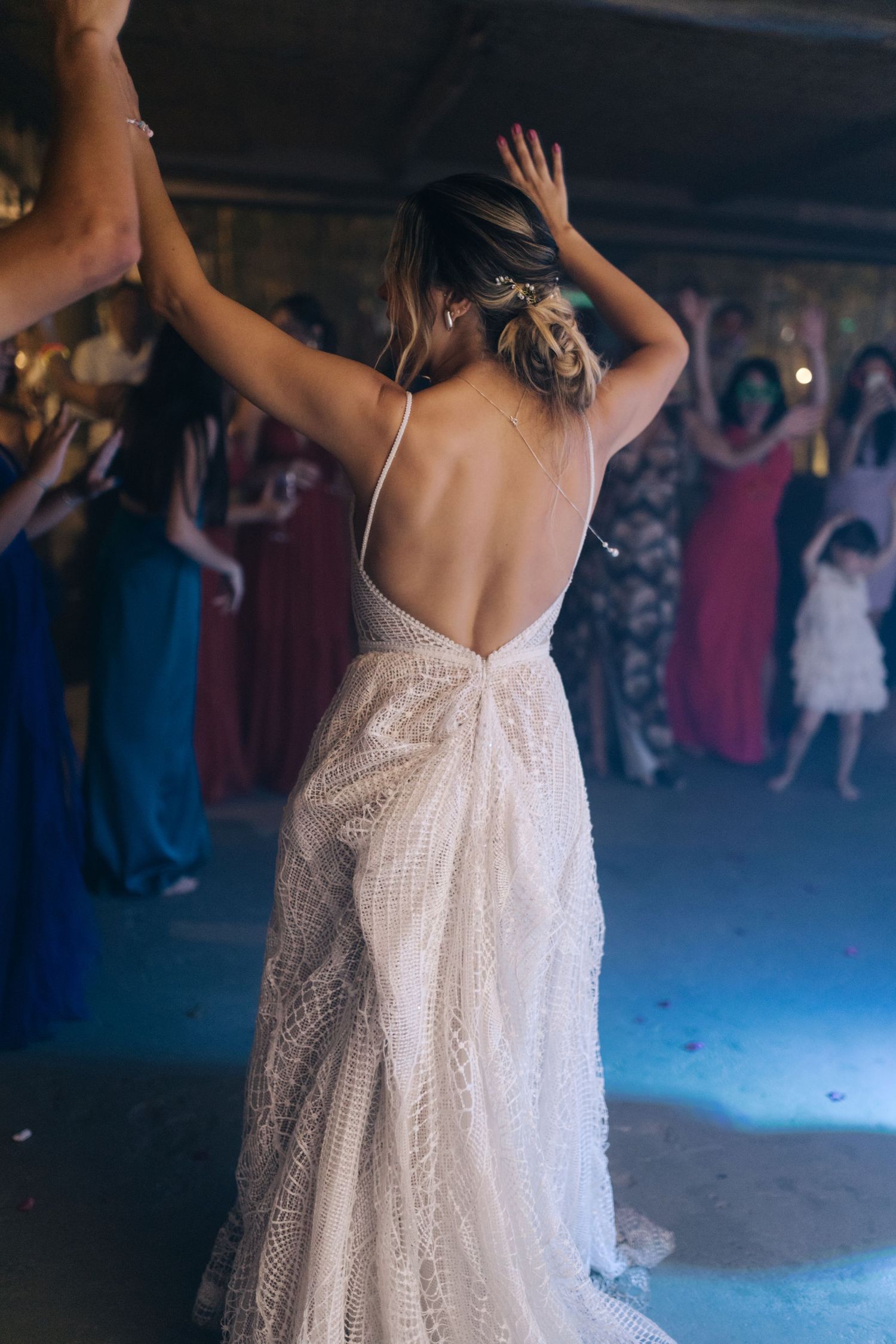 Back view of a bride in an open-back lace wedding dress dancing with arms raised.