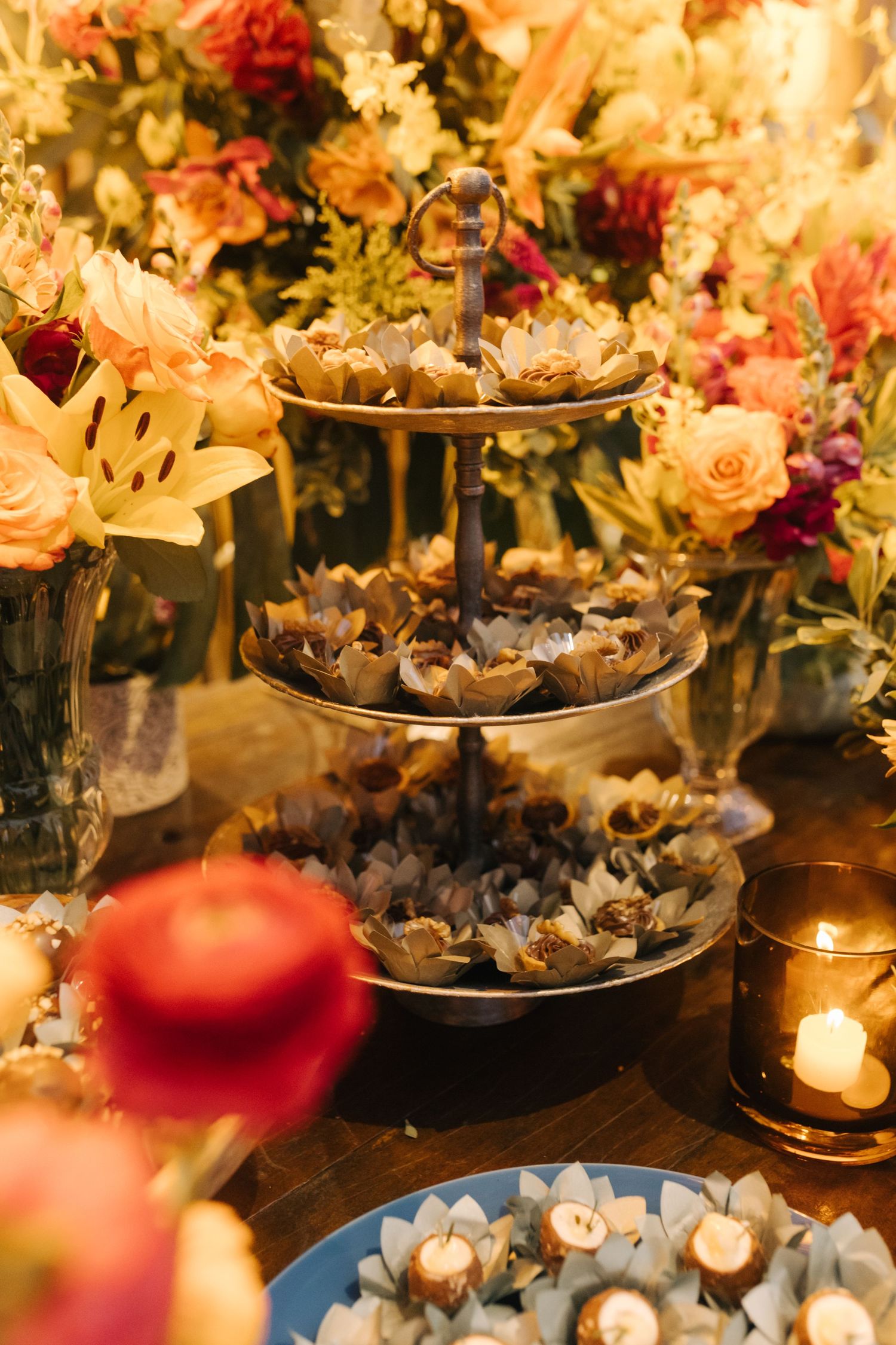 Multi-tiered display of wedding desserts surrounded by candles and lush floral arrangements.