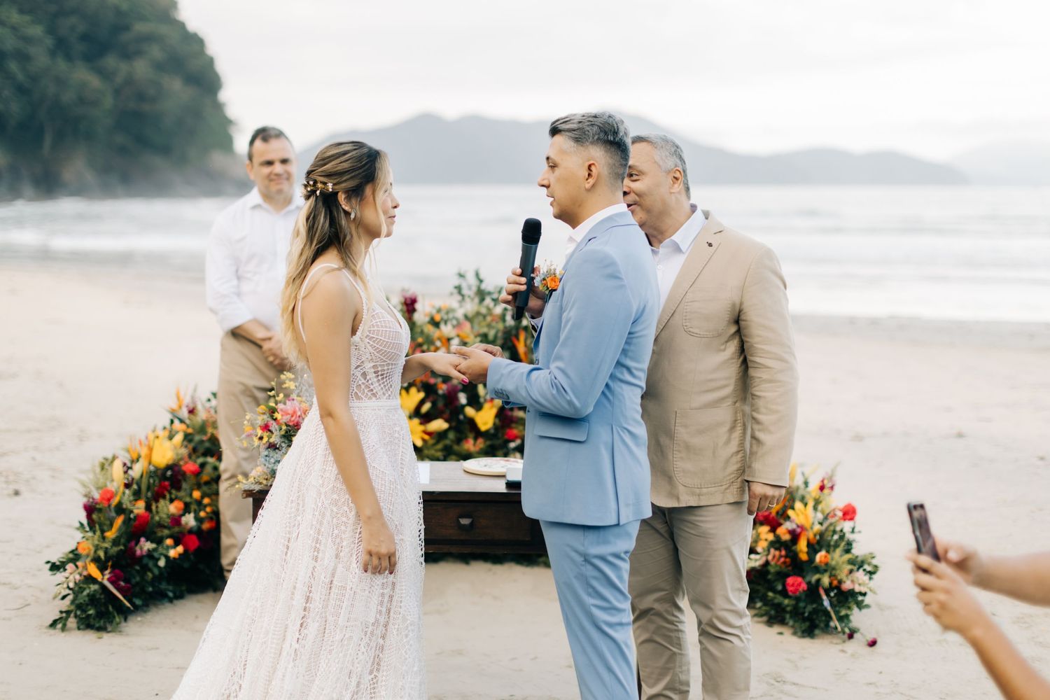 Beach wedding ceremony with colorful floral arrangements and guests in attendance.