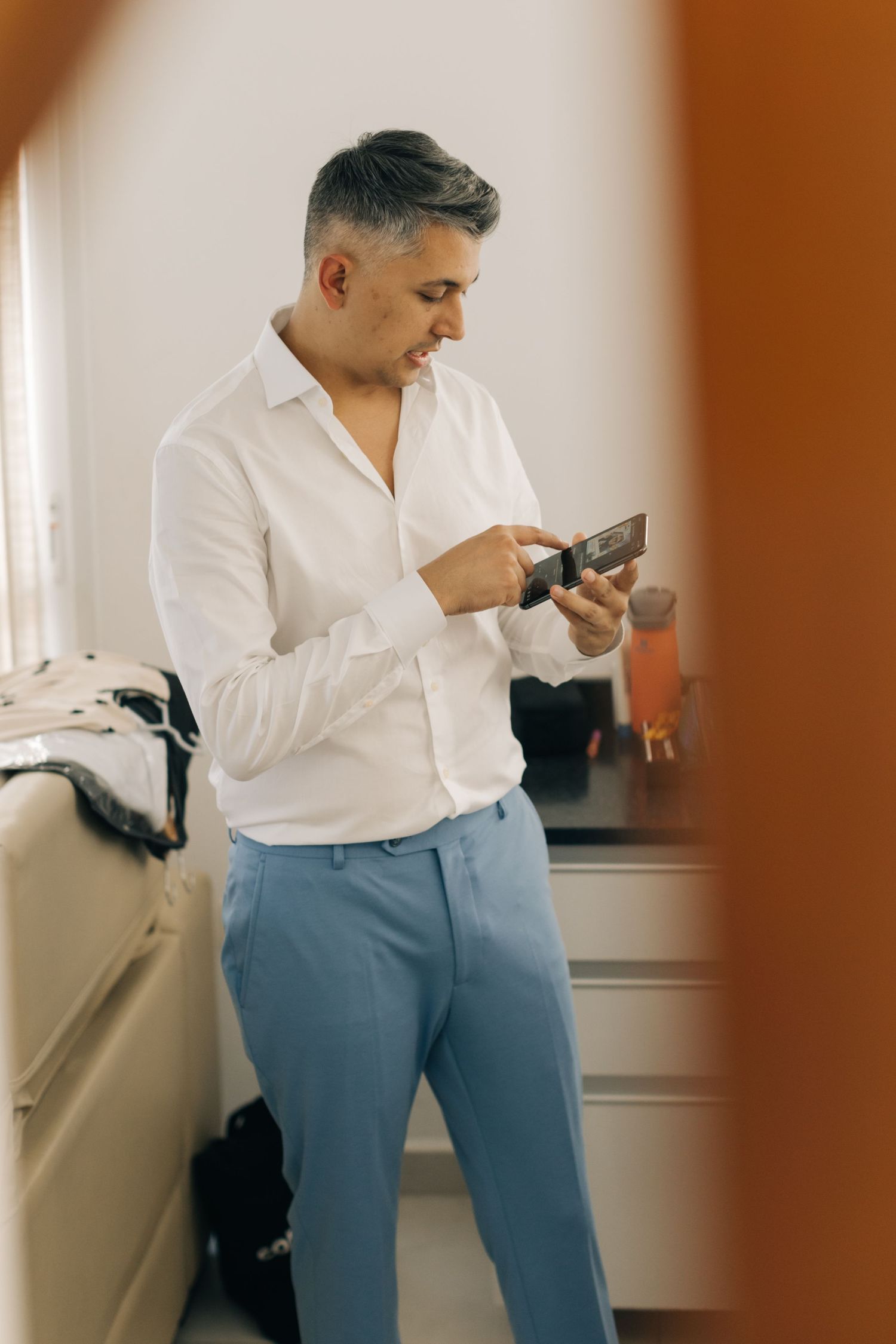 Man in white shirt and blue pants checking his phone in bright interior.