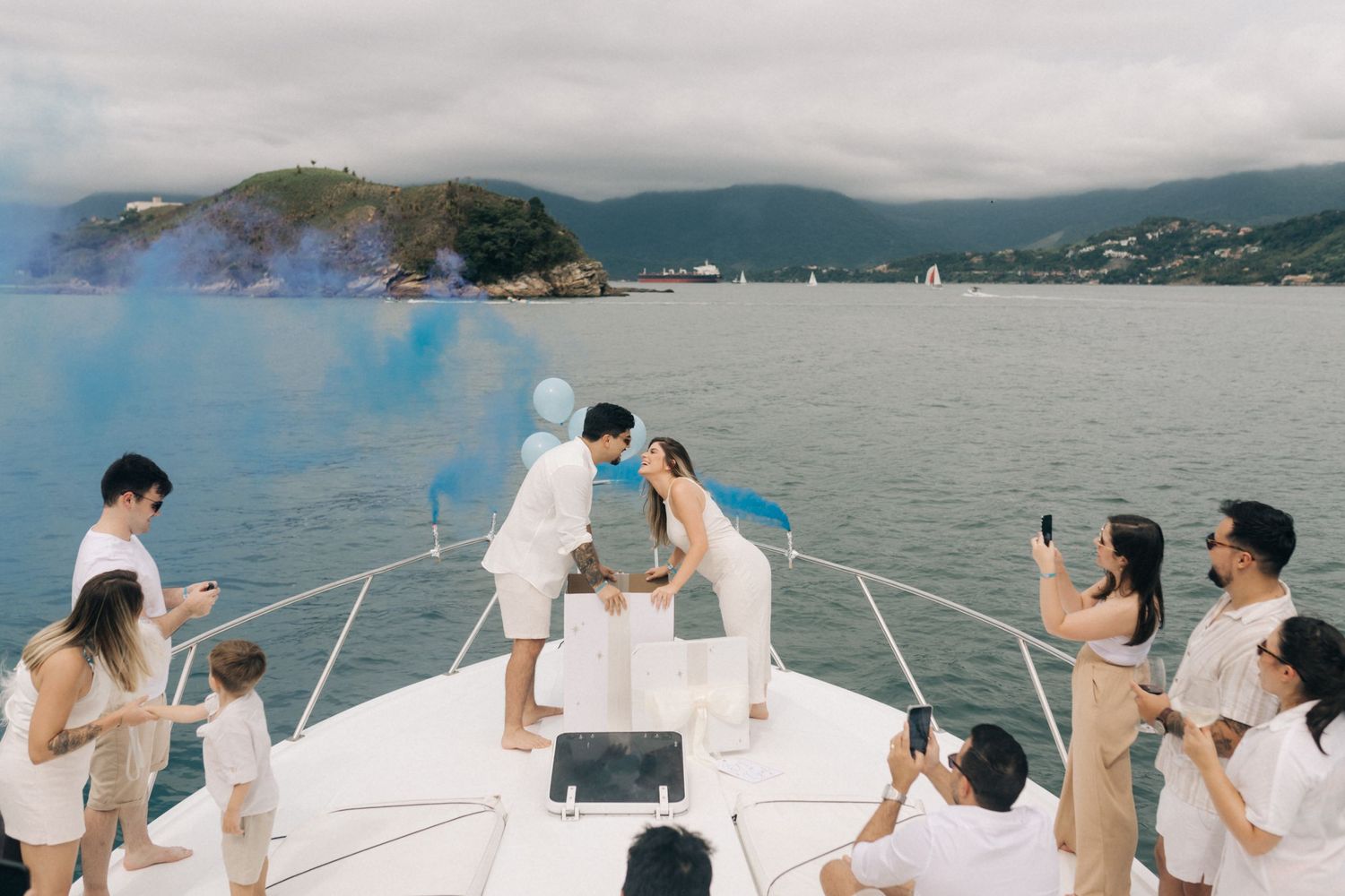 People celebrate with colorful smoke effects on a luxury boat with scenic mountain views.
