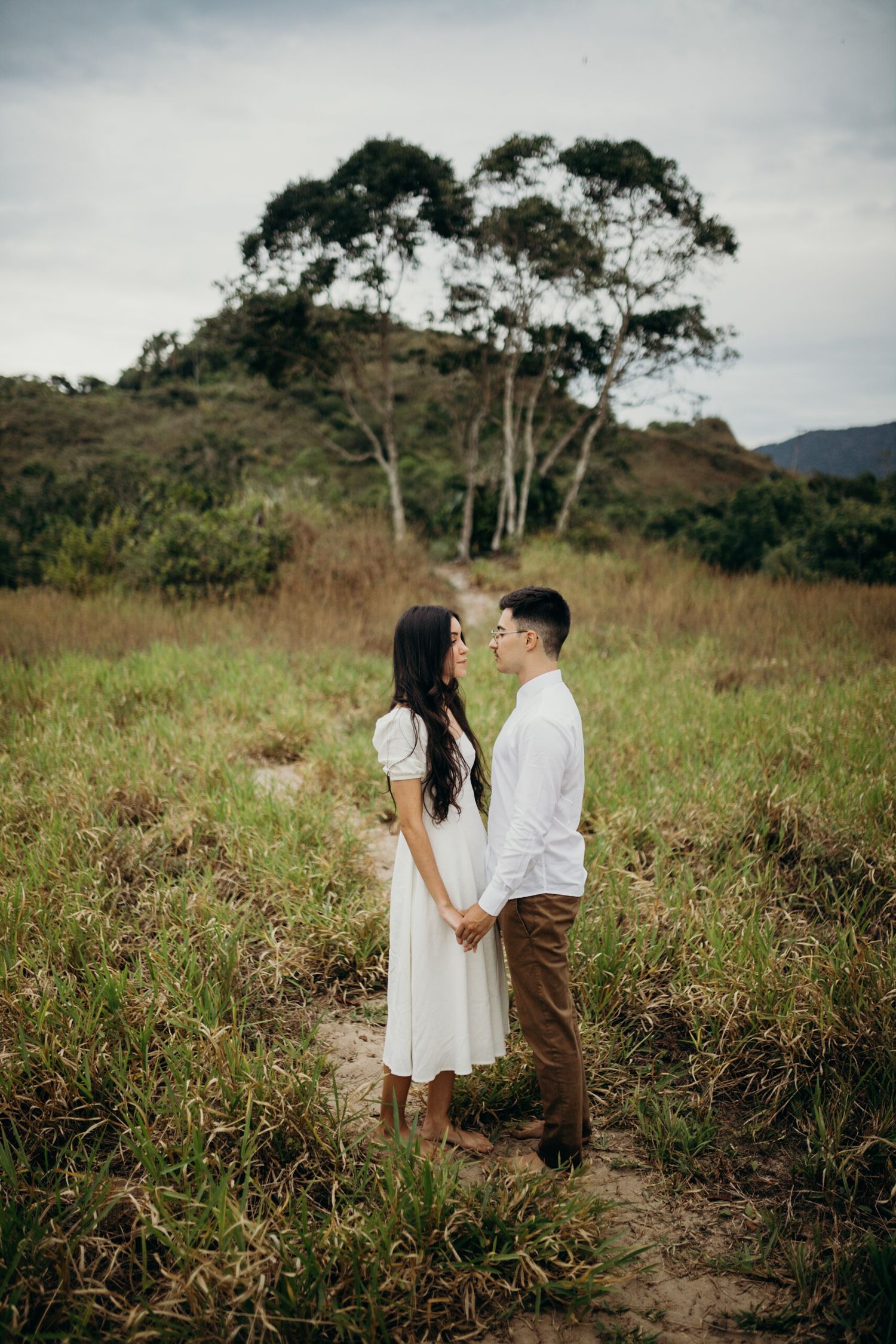 A couple sharing an intimate moment while standing in a grassy field with trees in the background.