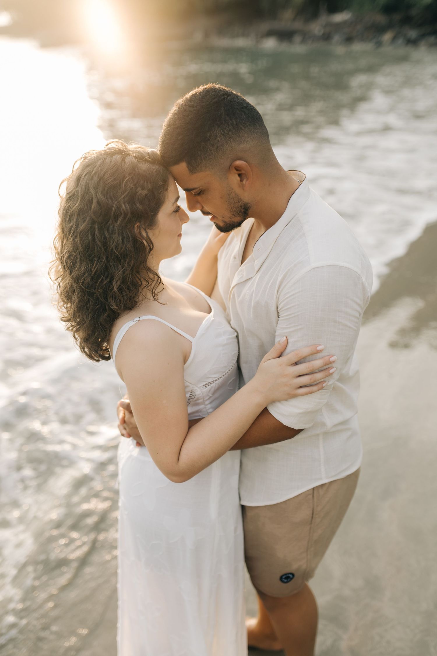 A tender moment between a couple in white clothing on a serene beach.