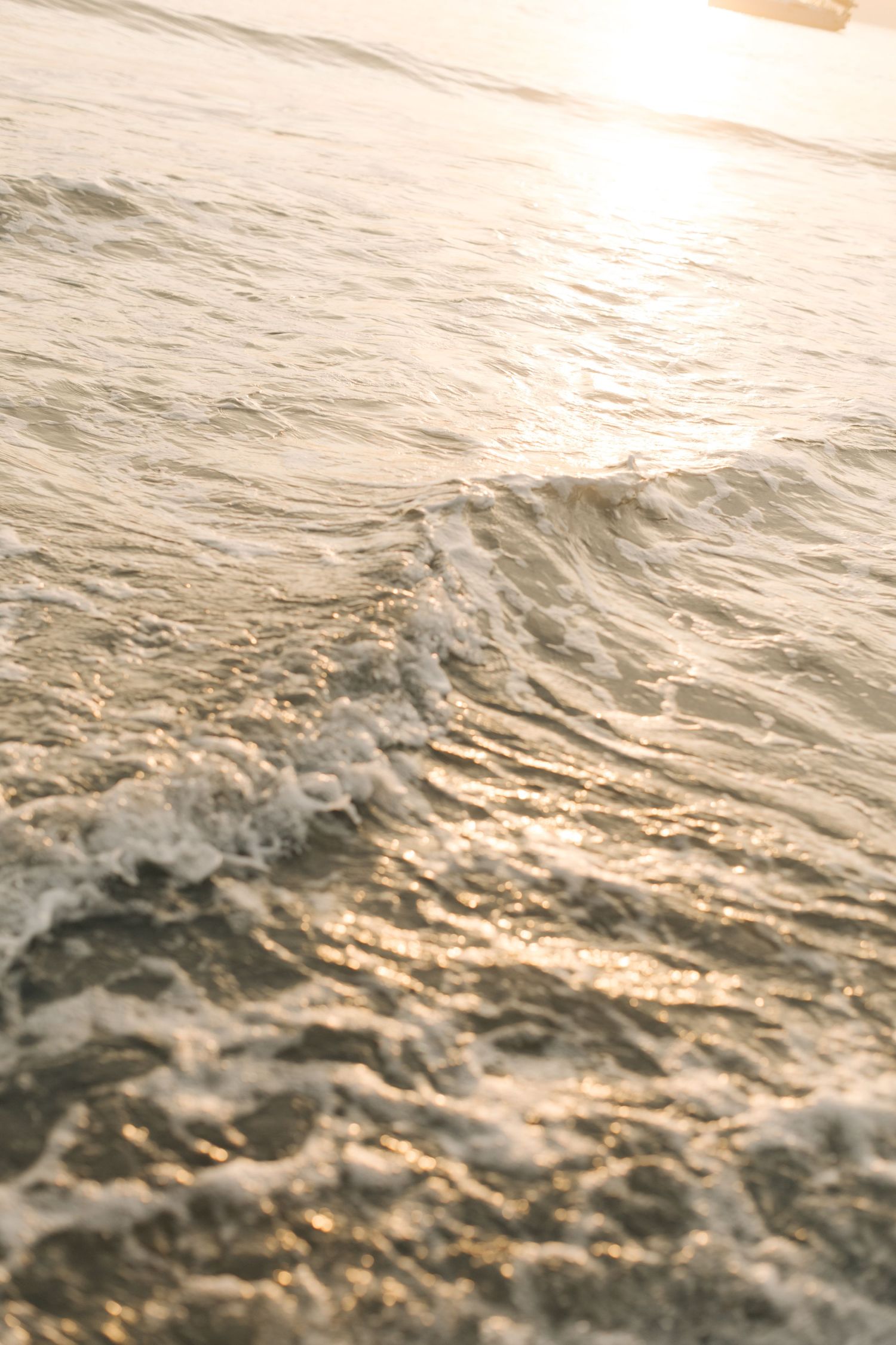 Ocean waves glisten with golden sunlight on a calm sea during sunset.