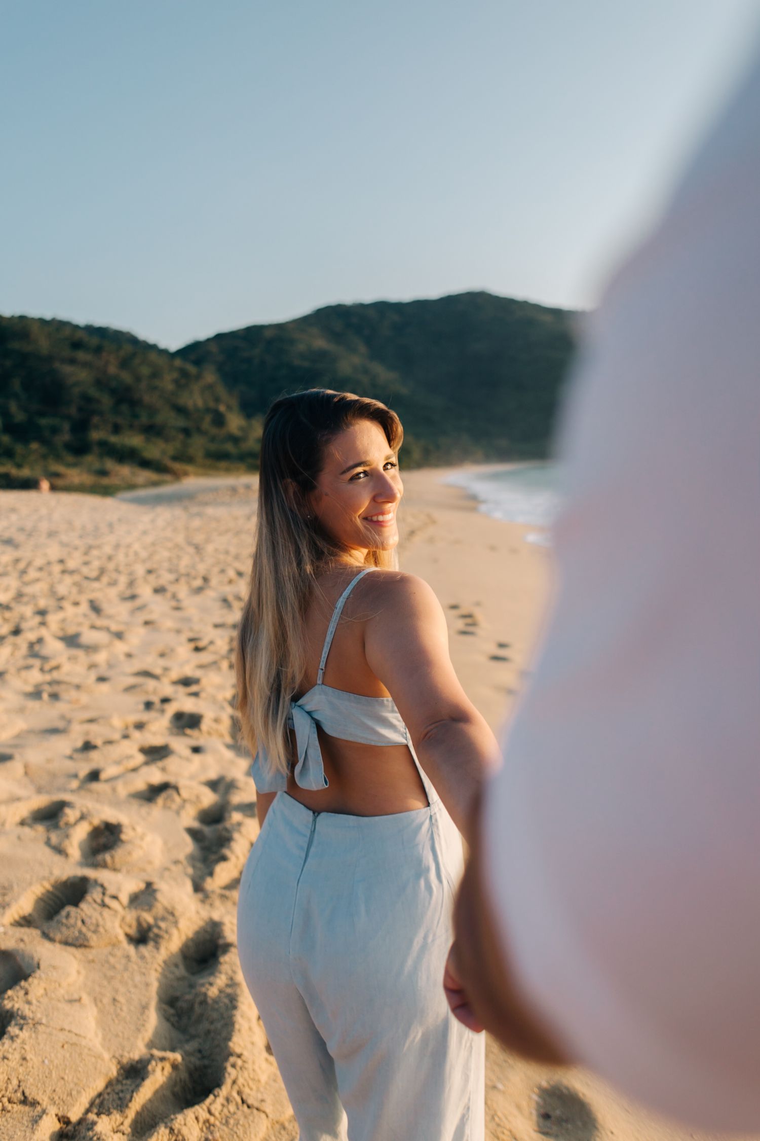 Woman in white beach outfit poses against coastal landscape during golden hour.