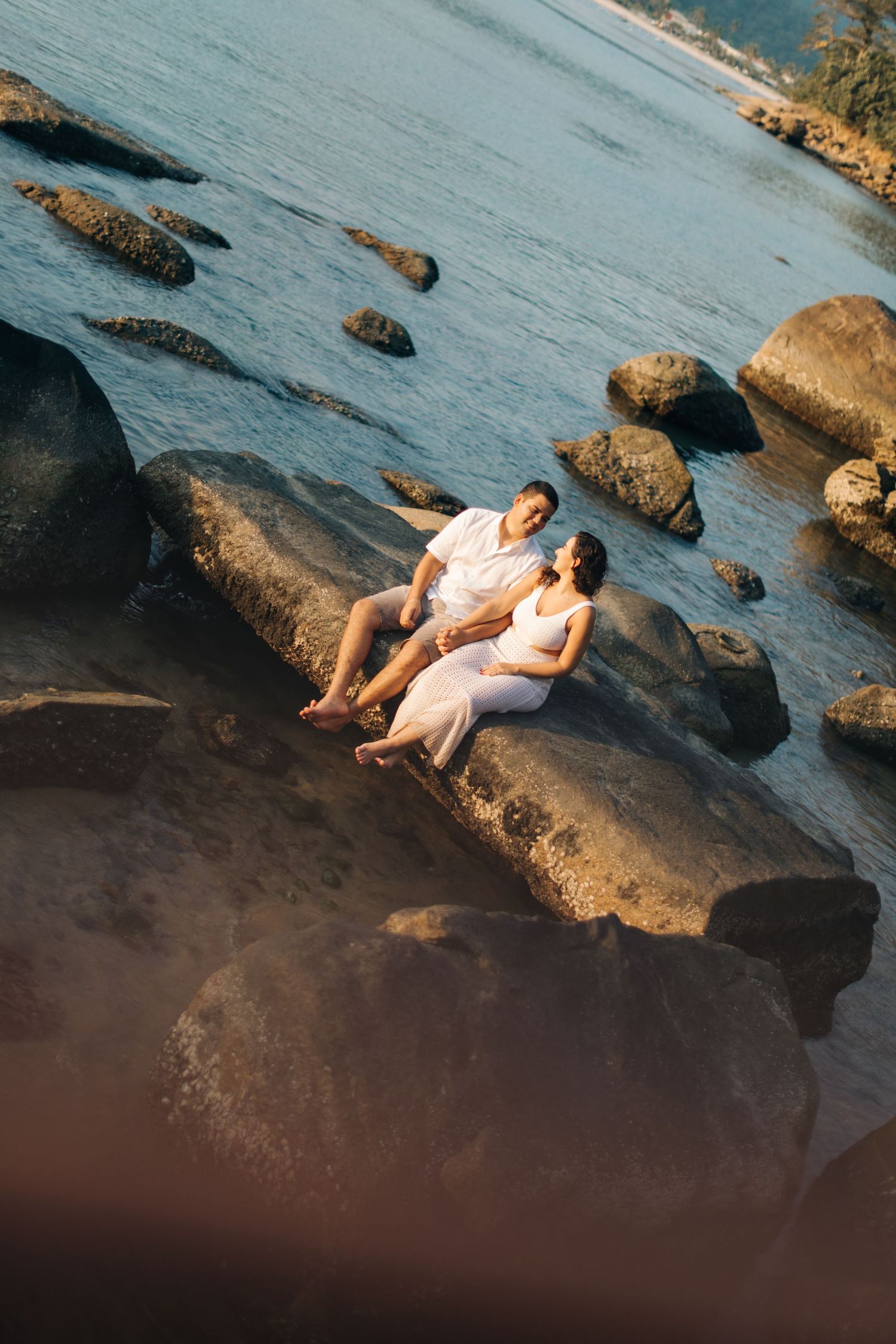 Couple relaxing on large rocks by the ocean during a sunny day.