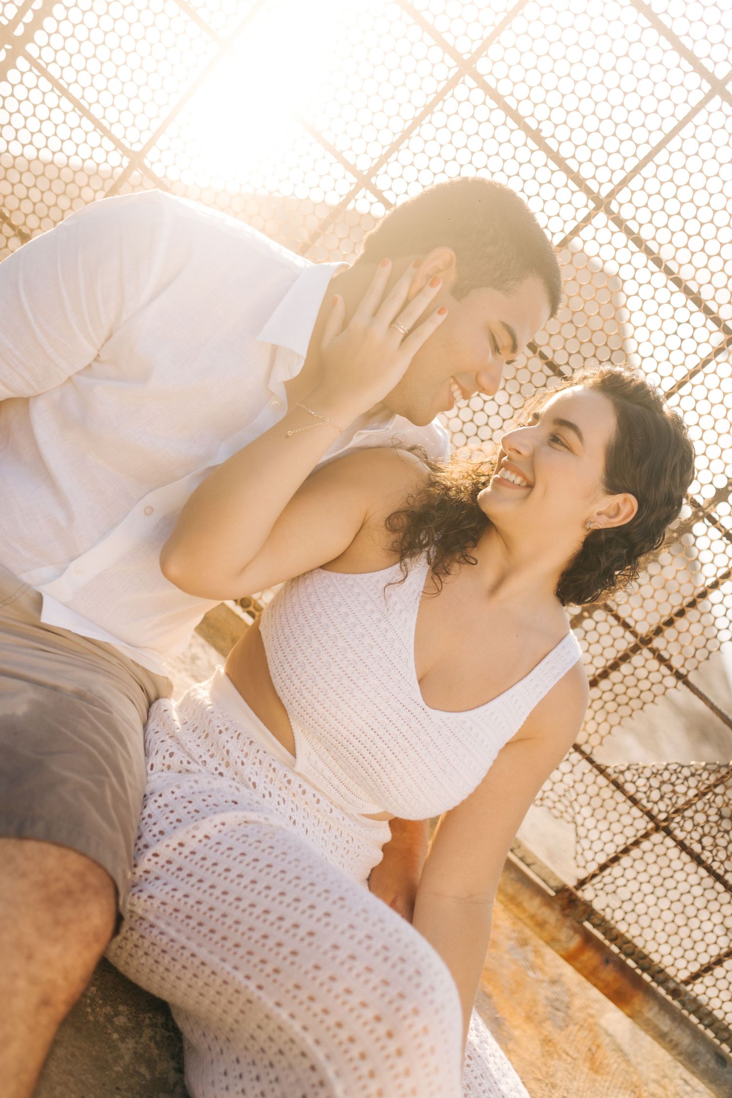 Romantic couple in white clothing sharing a joyful moment against a geometric patterned background.