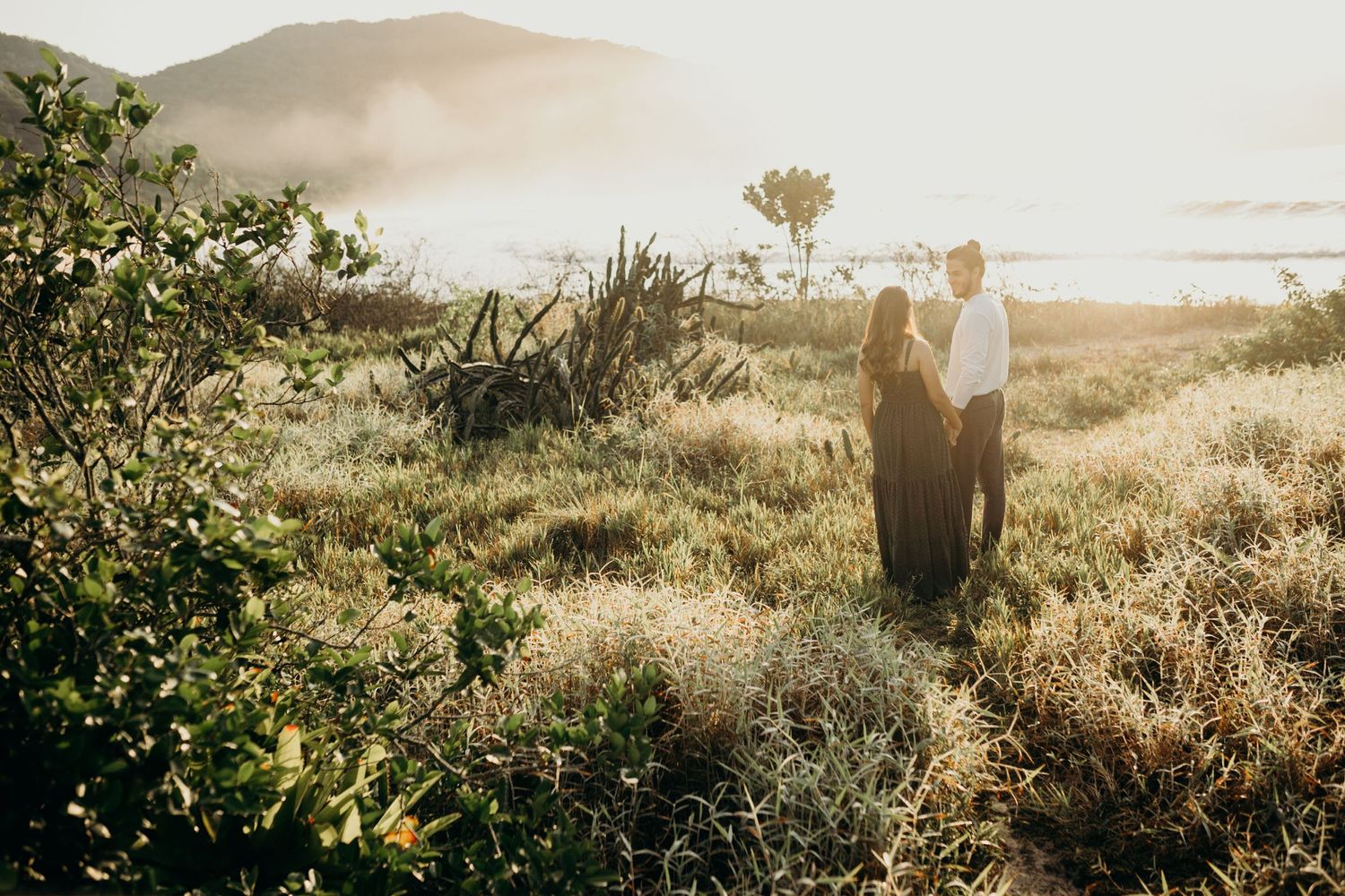 Couple holds hands while walking through mountain landscape at sunset.