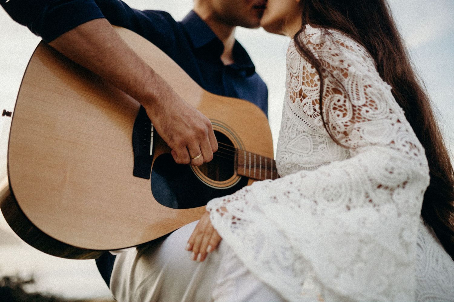 Close-up detail shot of hands on an acoustic guitar with white lace dress in frame.