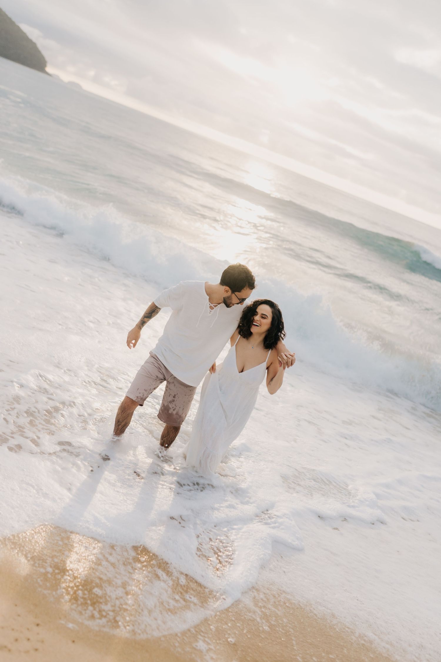 A couple plays in the ocean waves during a beach photoshoot.
