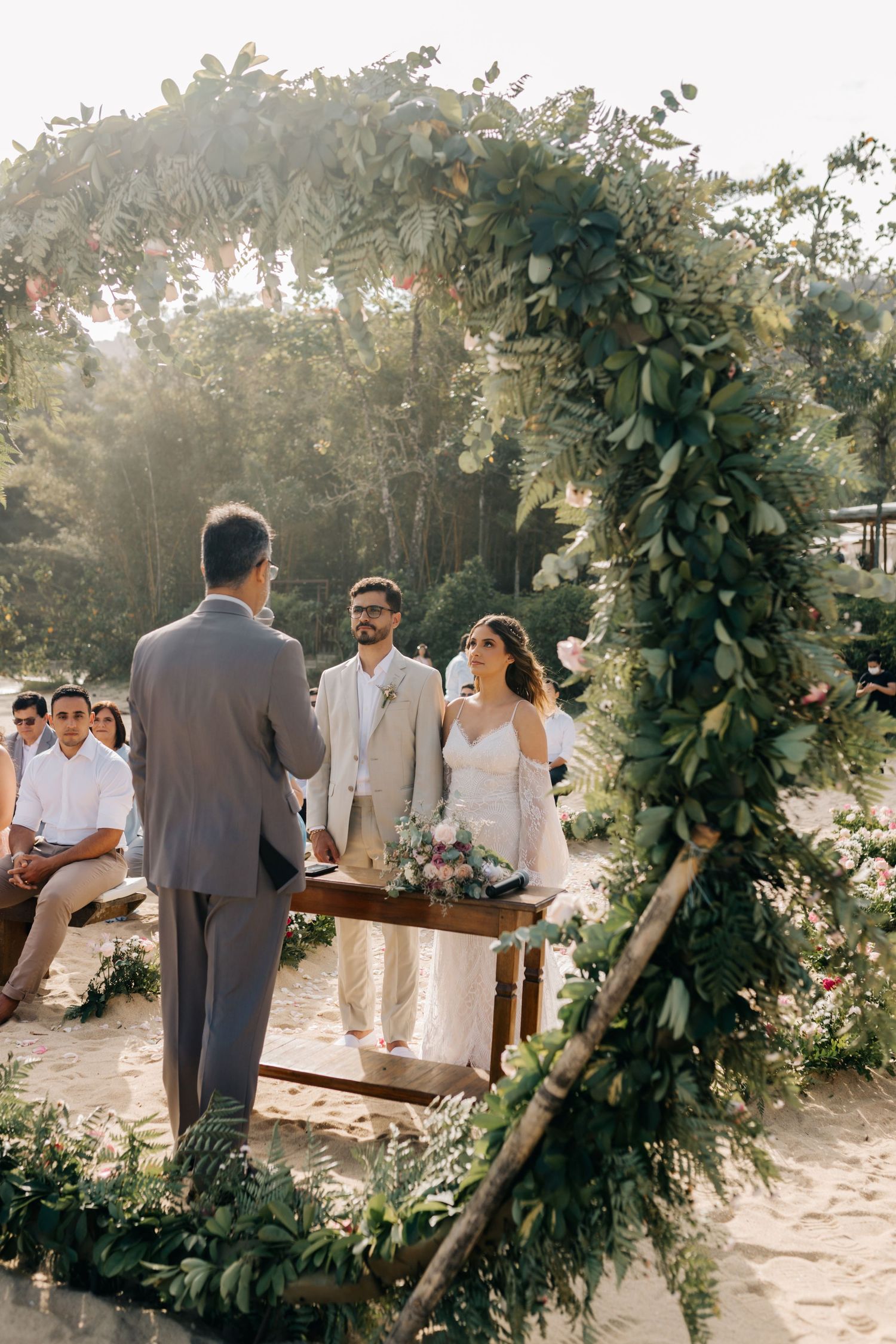Beach wedding setup with wooden benches and natural greenery archway decorations.
