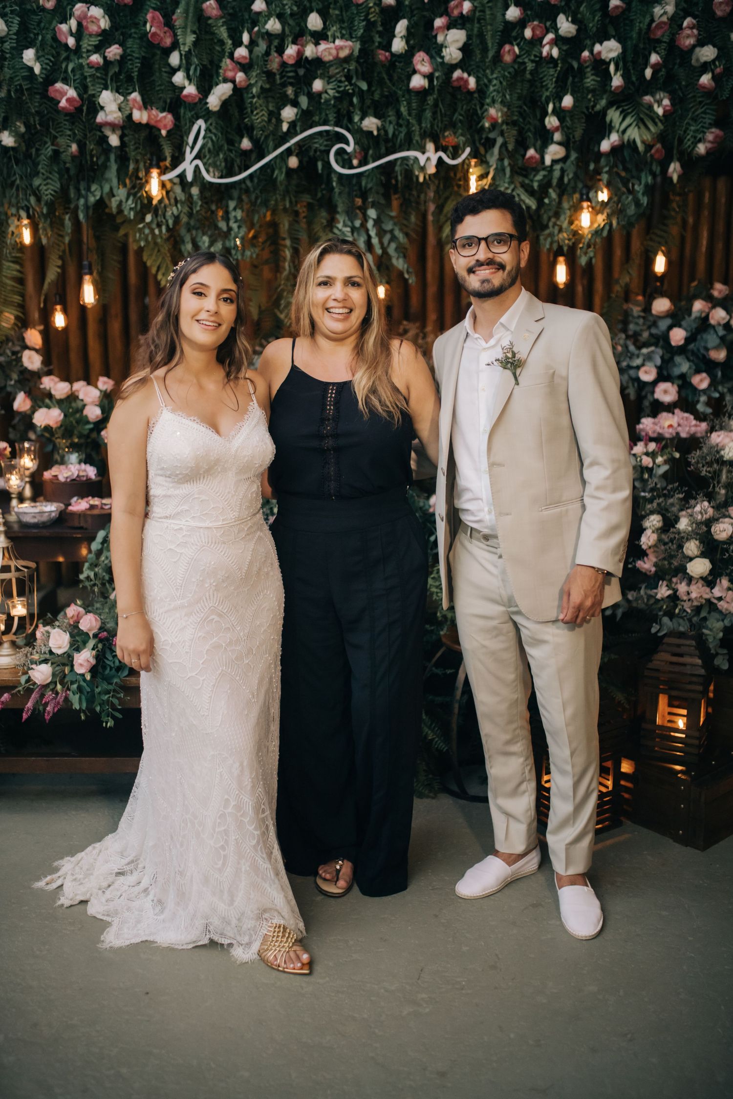 Wedding photo with formal group against floral wall backdrop with hanging lights.