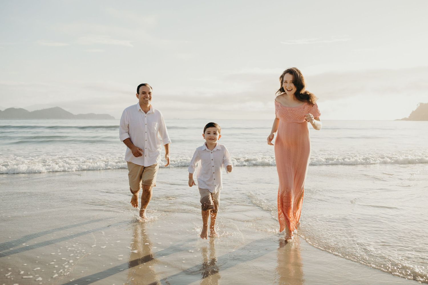 Family running together along wet sand at the beach during golden hour.