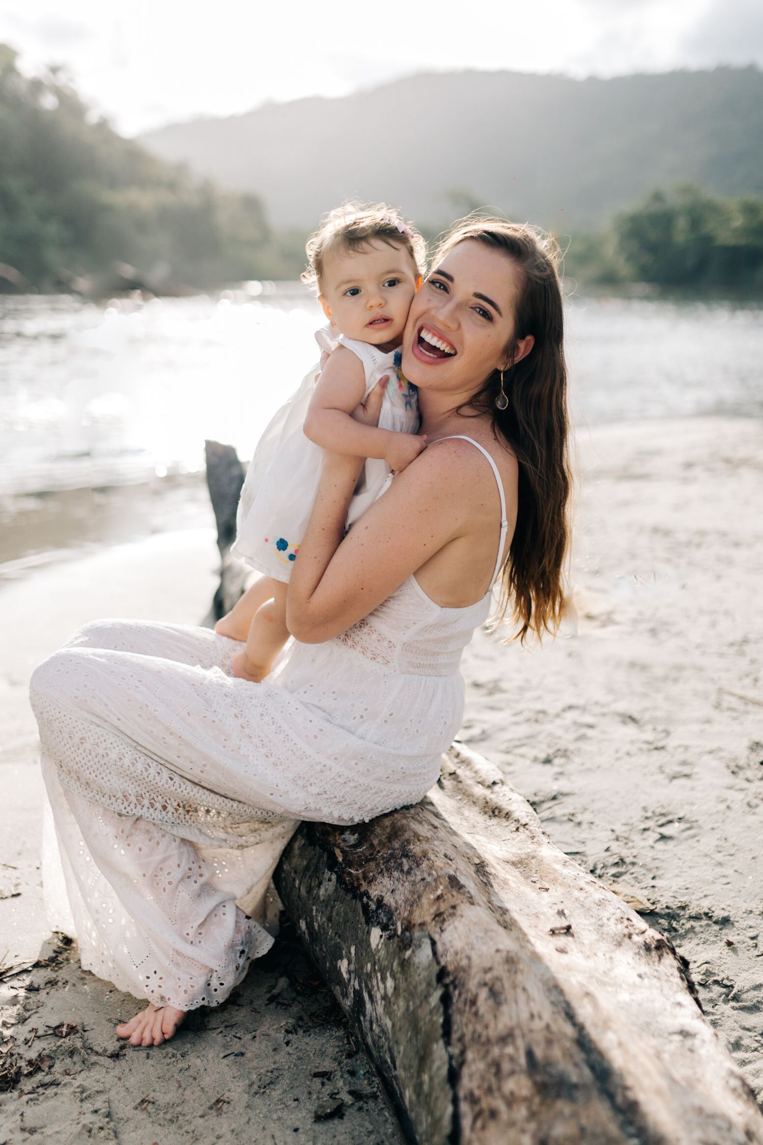 A loving moment captured between parent and child sitting on driftwood by the water.