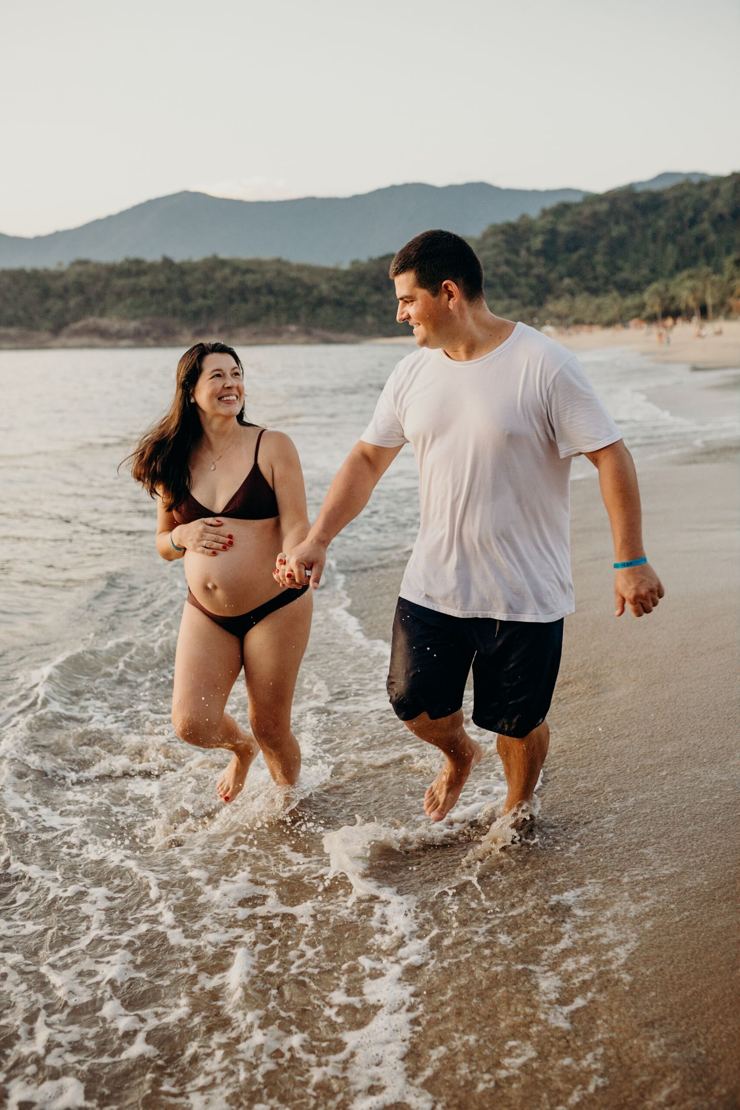 Joyful couple running through shallow ocean water with mountains in the background.