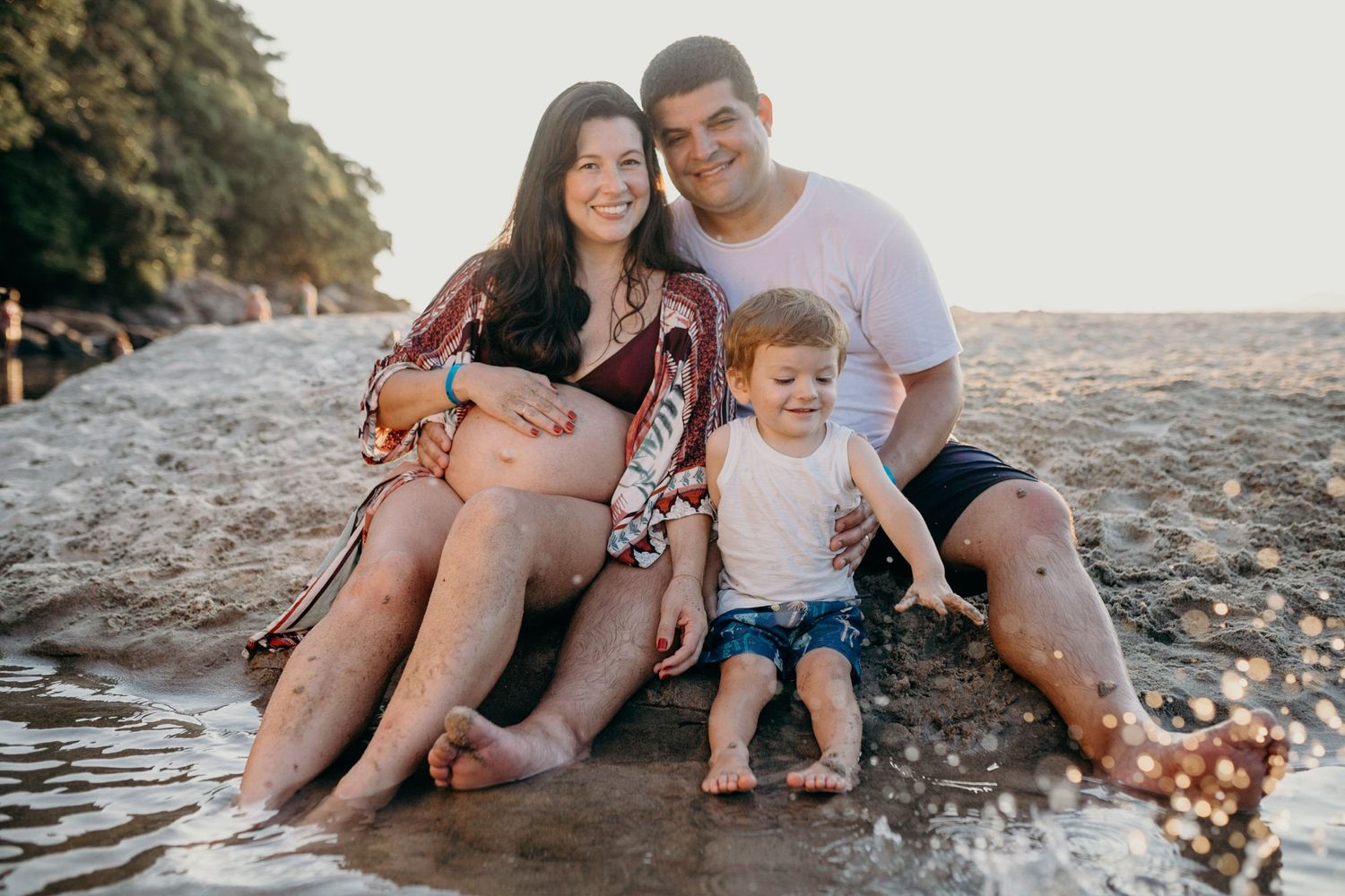 Family sitting together on rocky beach during golden hour.