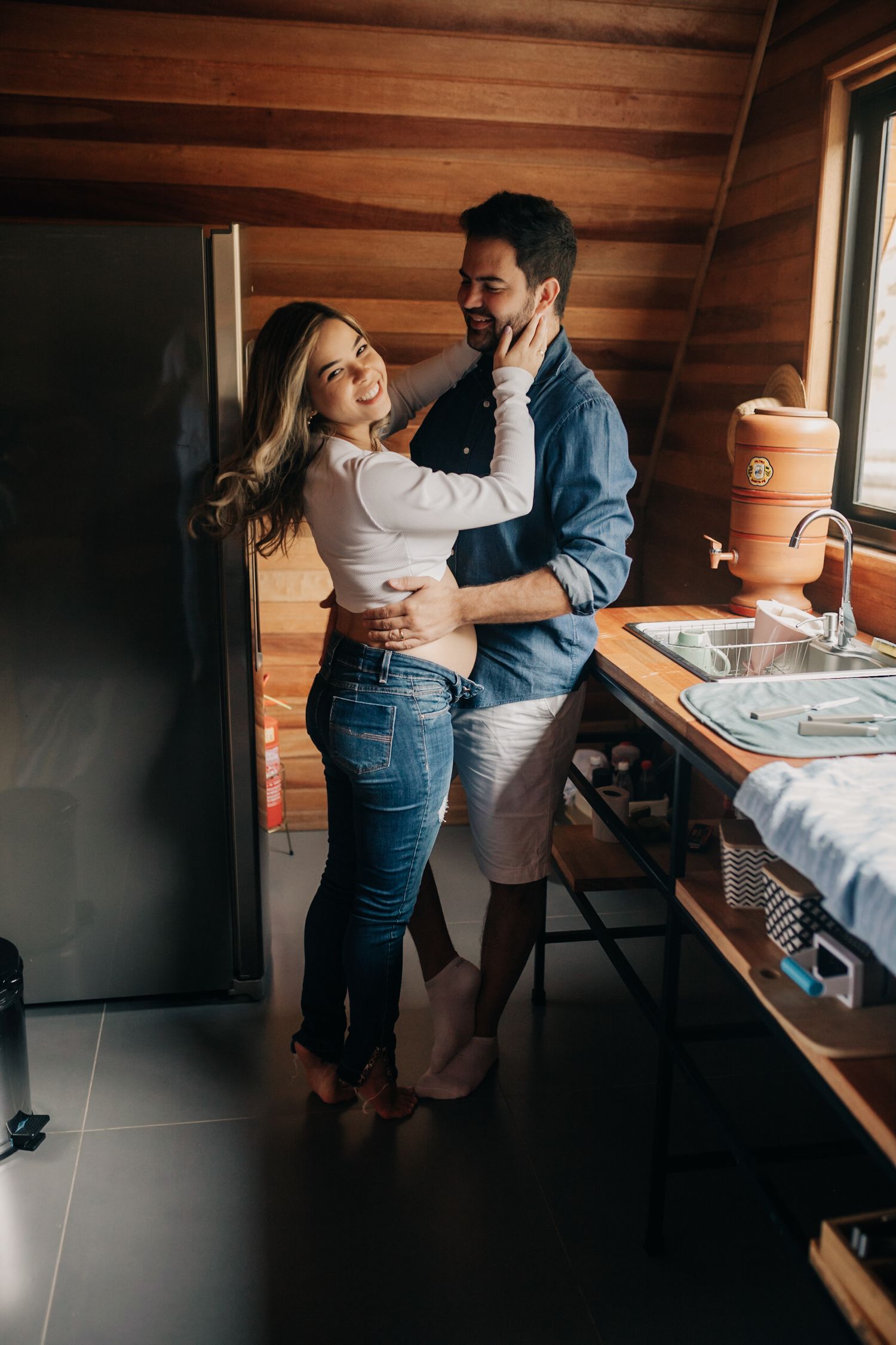 Couple embracing in a cozy corner with wooden walls and natural lighting.