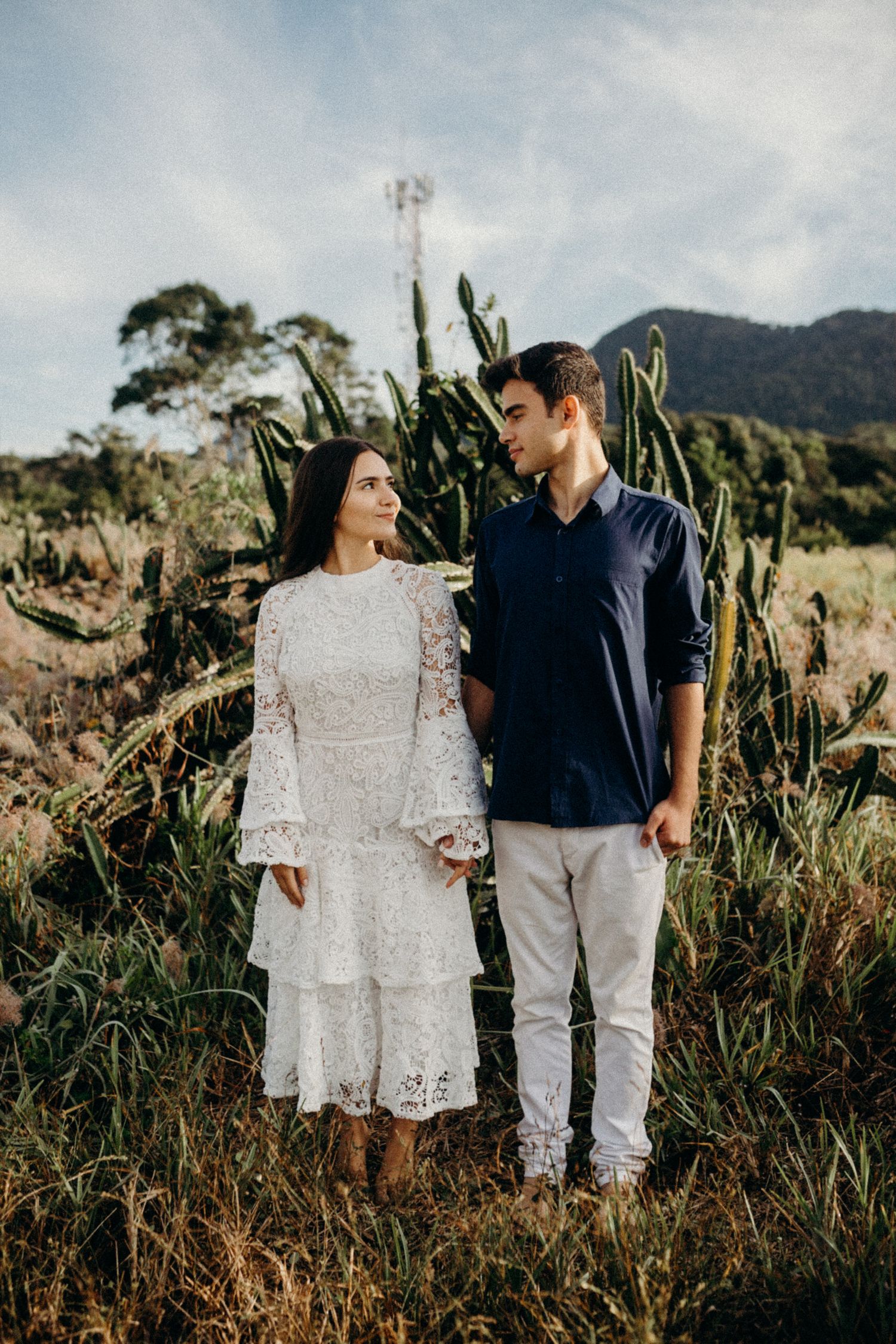 A couple stands in a field with mountains and native plants in the background.