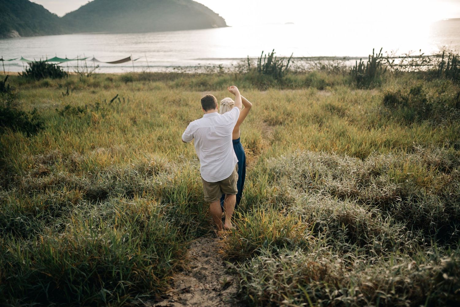 Couple strolling through a coastal meadow with mountain and ocean views.
