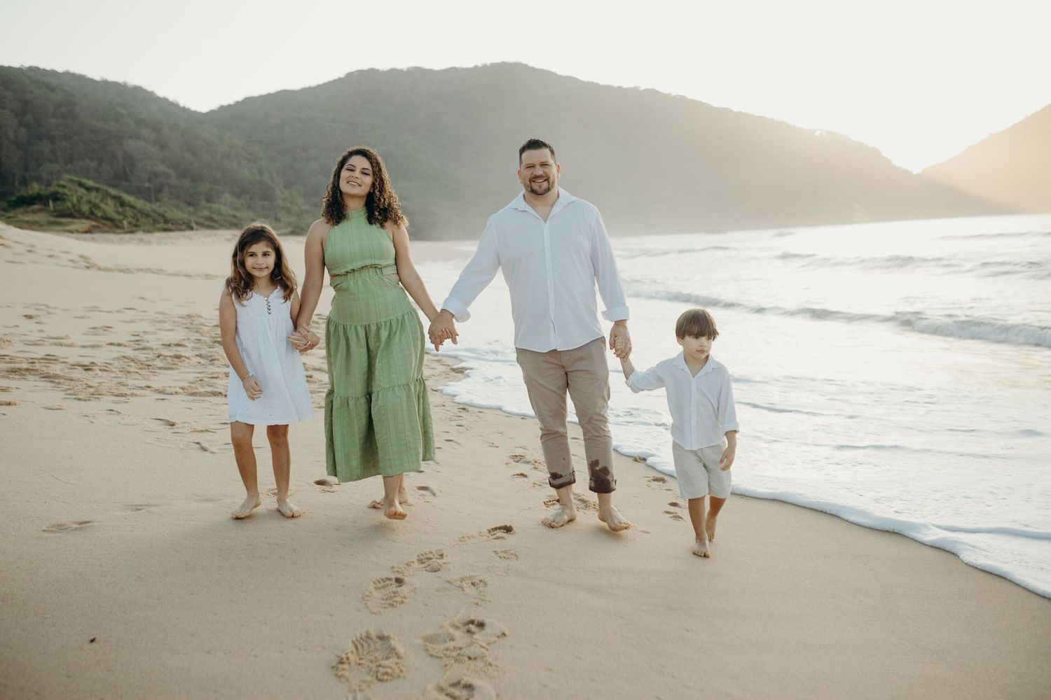 Family walking along a scenic beach at sunset with mountains in the background.