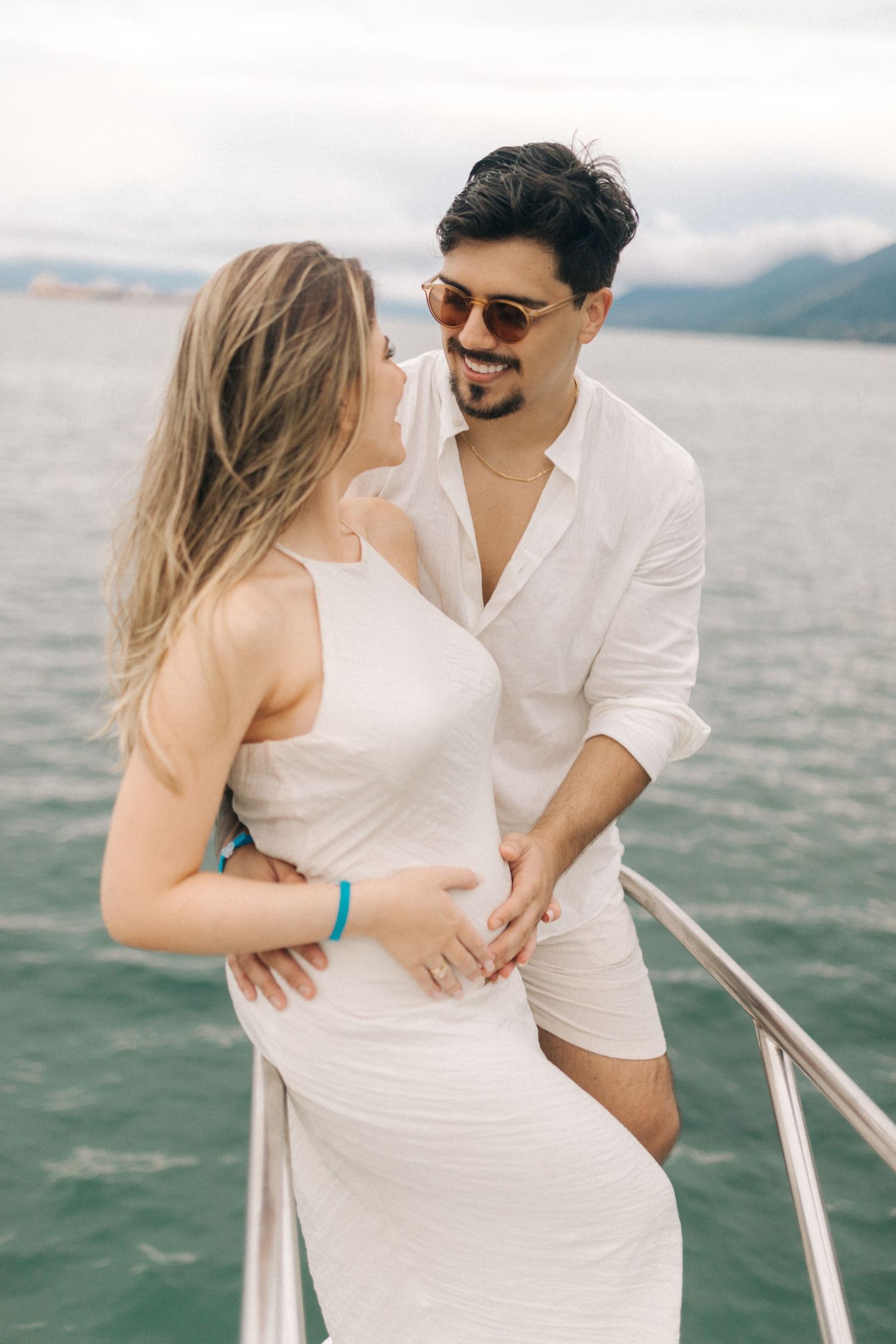 Couple in white outfits sharing tender moment on boat with ocean view.