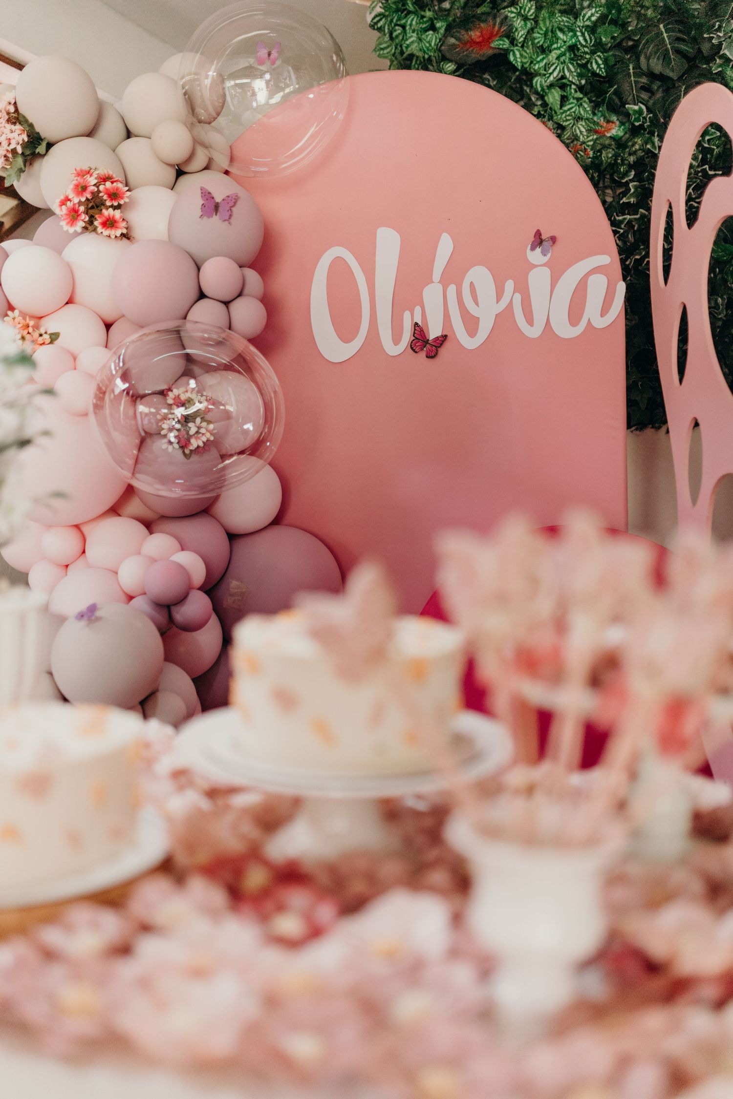 Pink balloon arch and party decor with name 'Olivia' on round backdrop.