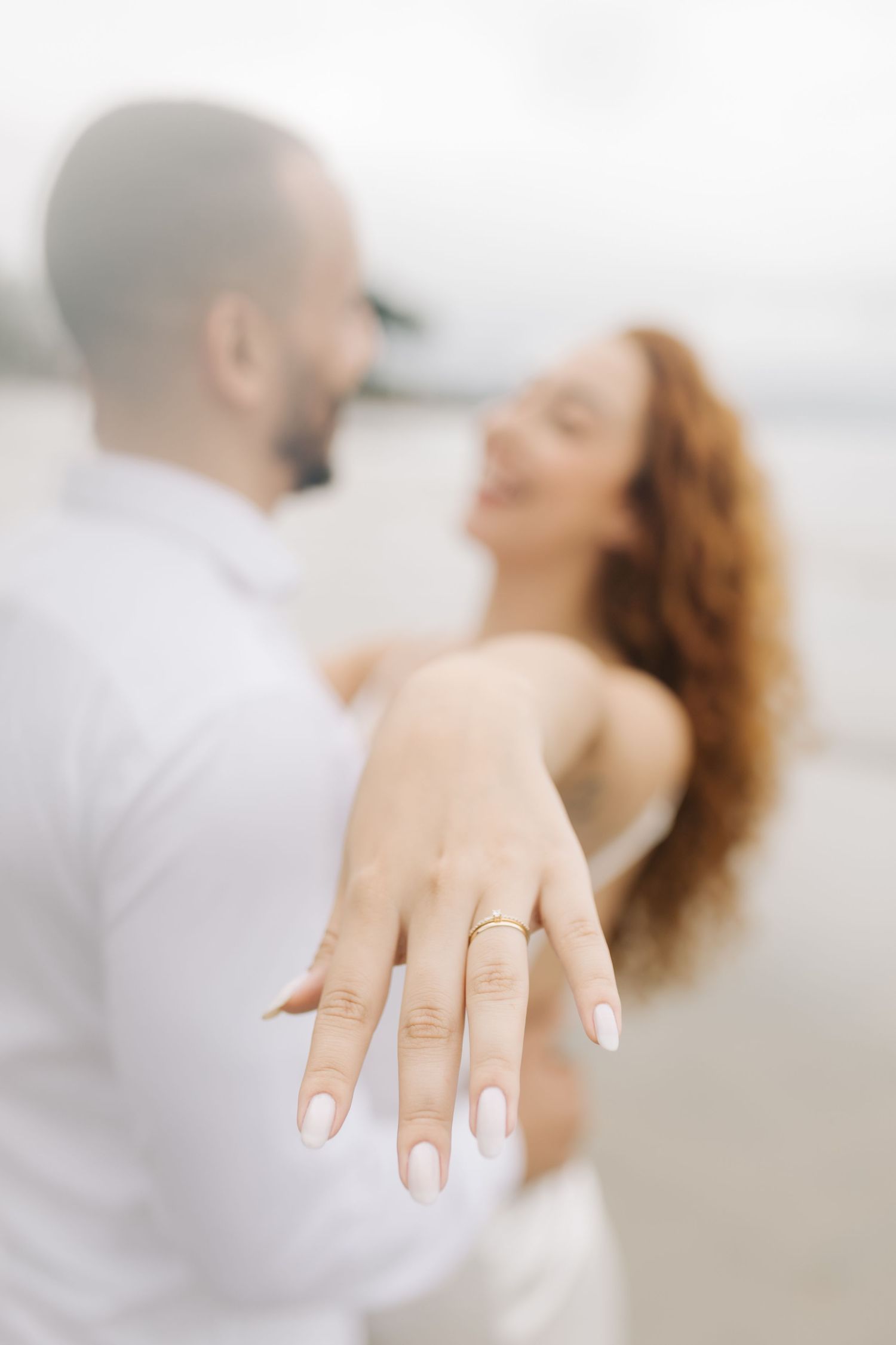 Beach engagement photo series highlighting a sparkling ring with couple embracing in background.